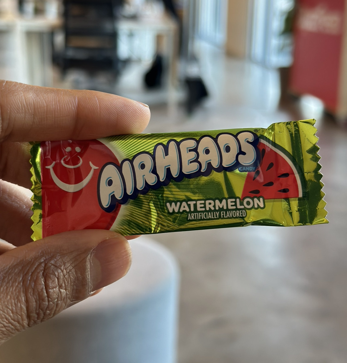 A hand holding a packet of Airheads Watermelon candy