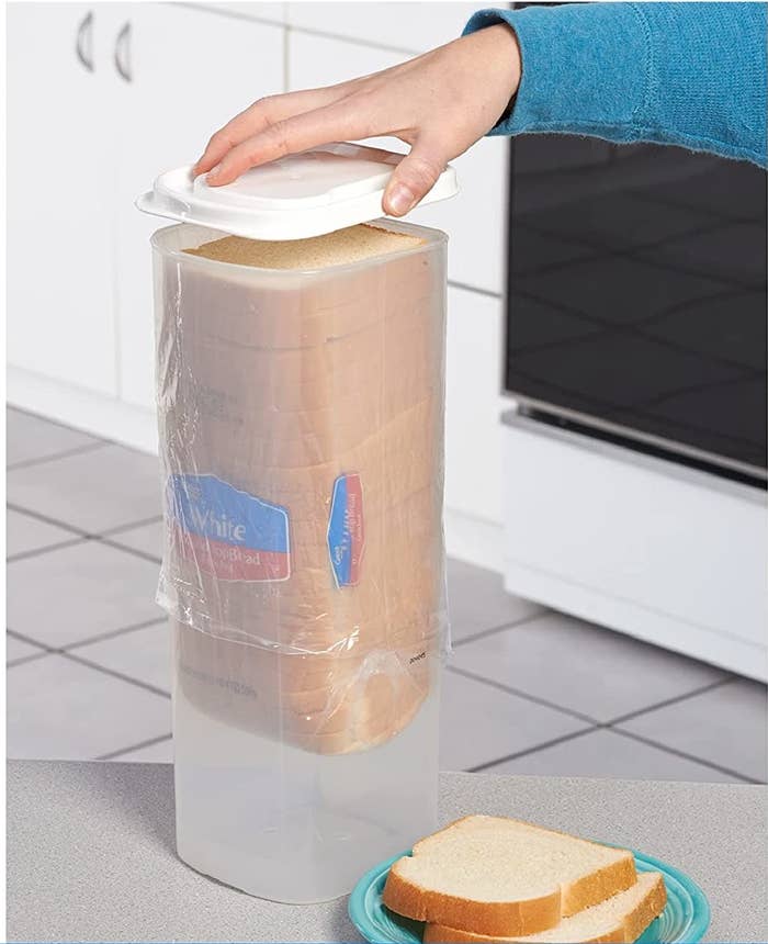 person putting a lid on the container that has a loaf of bread in it and a plate of bread next to it
