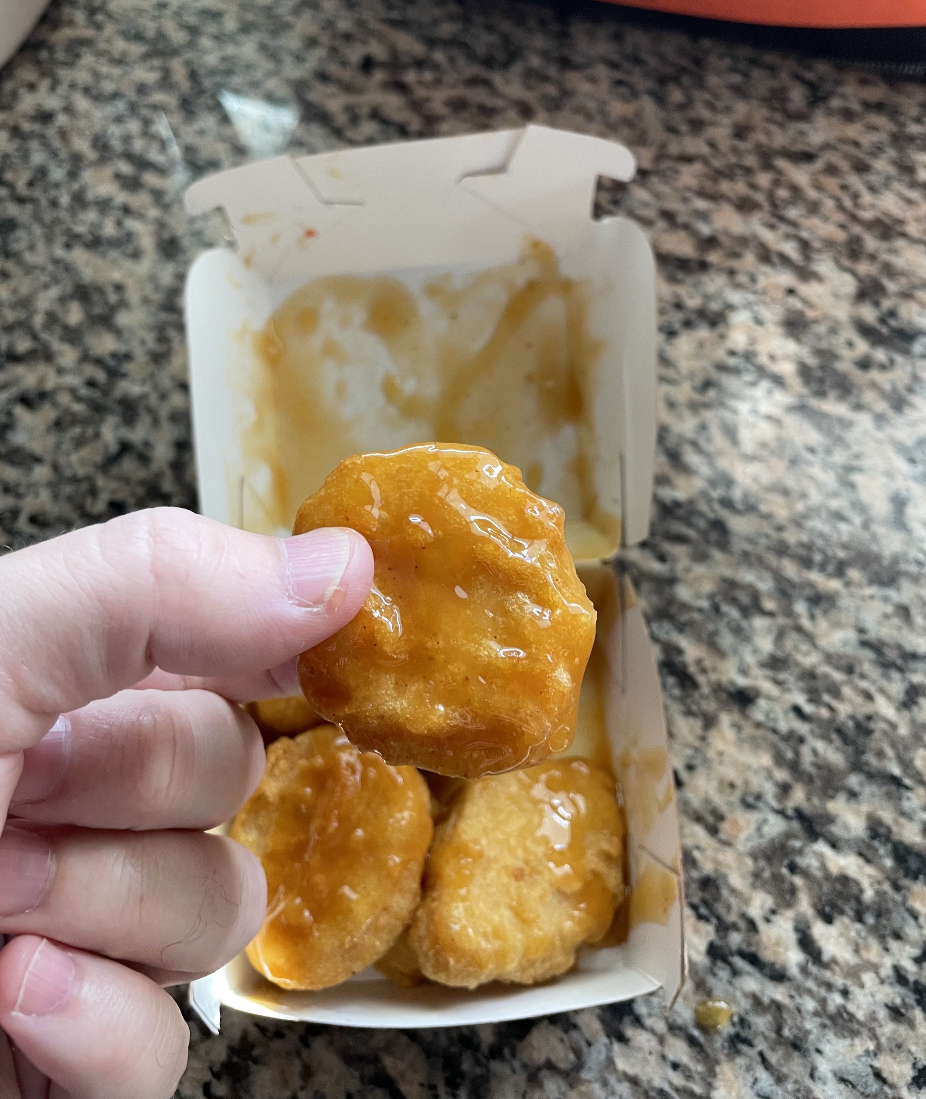 Hand holding a nugget with sauce on it