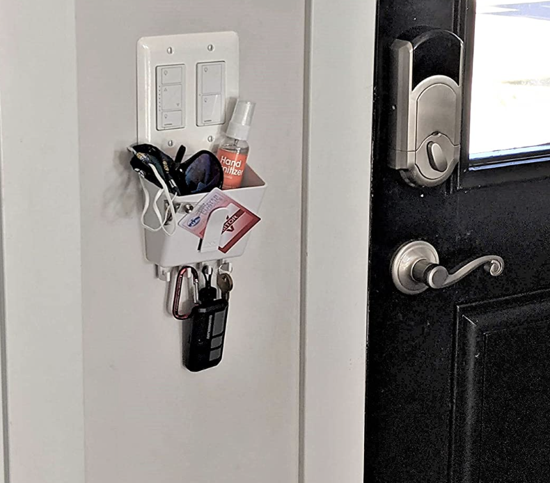 the basket hanging from a switch next to a front door holding keys and hand sanitzier