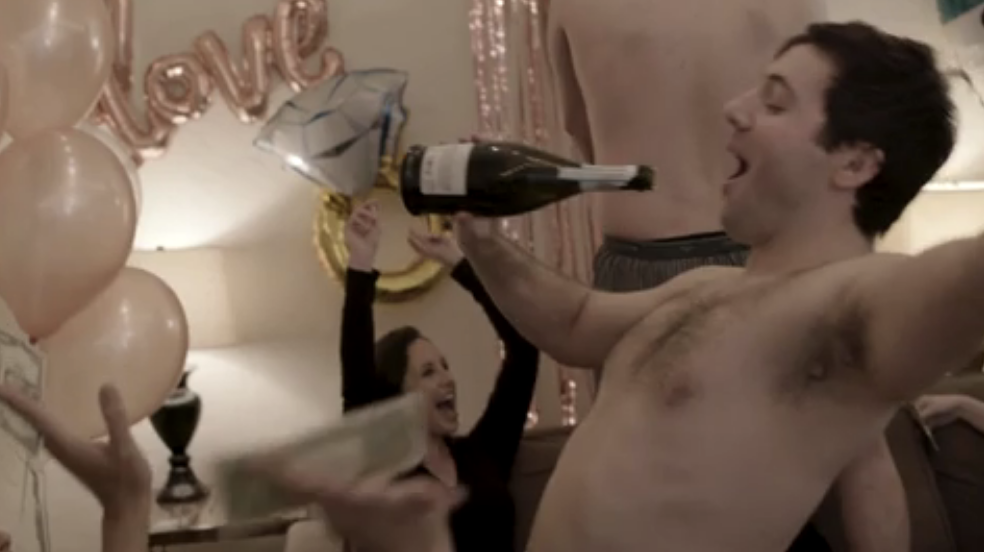A shirtless man with a champagne bottle