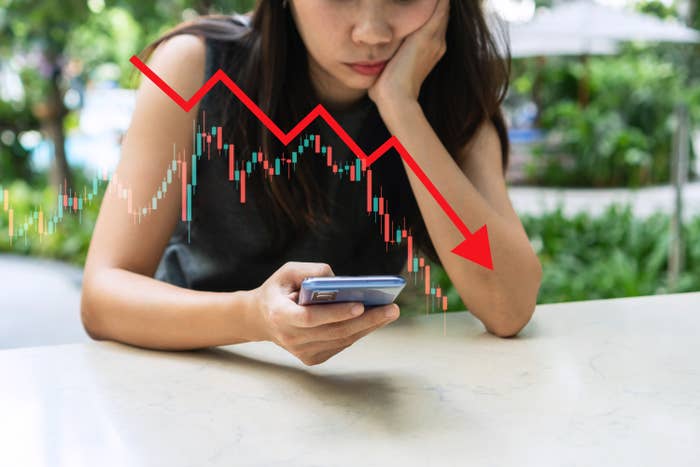Stressed Asian businesswoman crypto looks at mobile phone analyzing stock exchange market