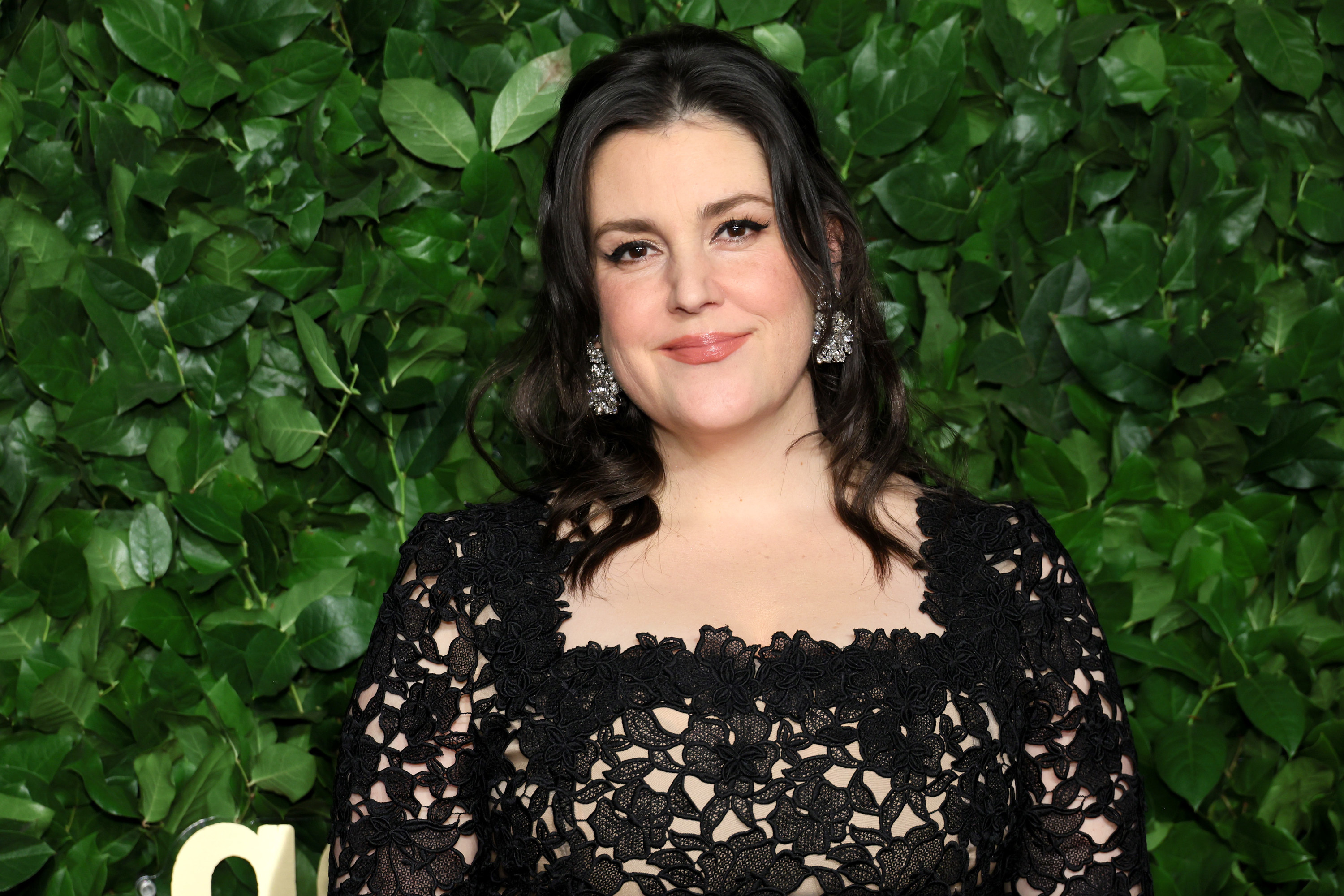 Melanie Lynskey posing for a photo in front of a wall of green leaves