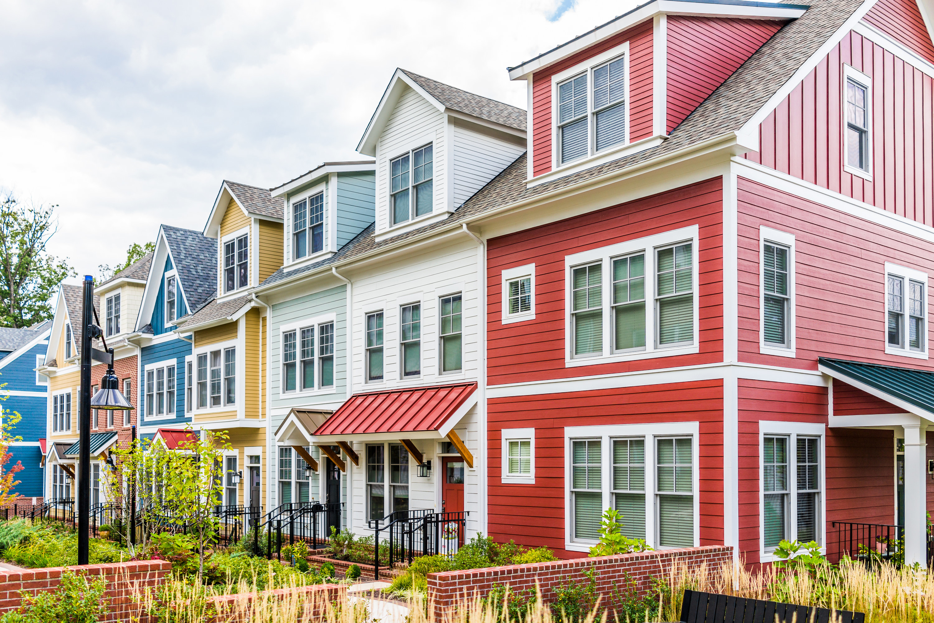 Row of colorful, red, yellow, blue, white, green painted residential townhouses, homes, houses with brick patio gardens in summer in Maryland