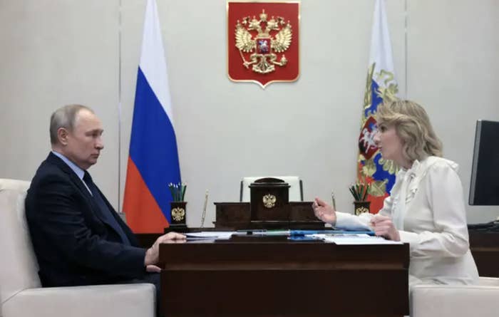 Vladimir Putin and Maria Lvova-Belova sit across from each other at a desk