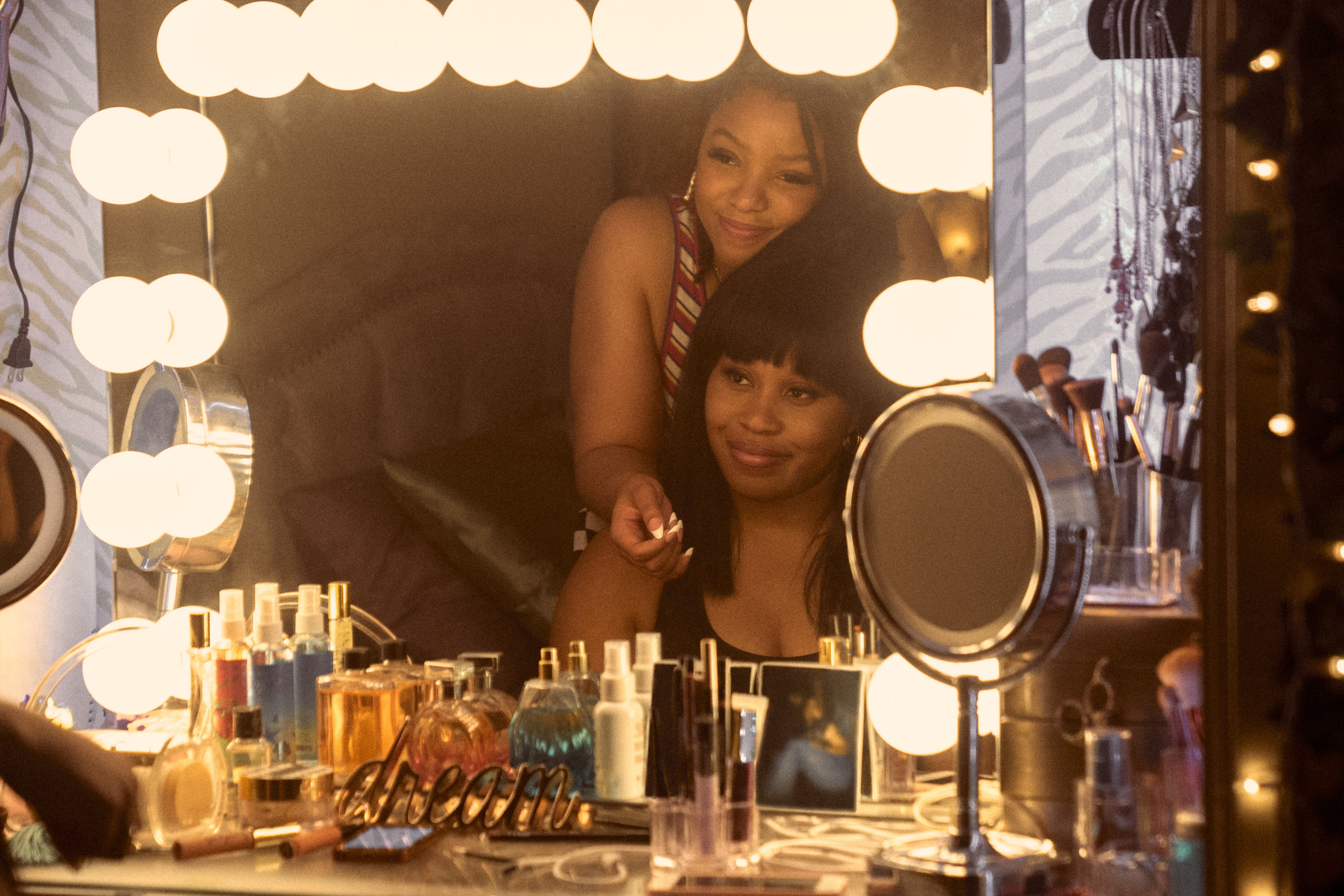 Dominique looking into a vanity mirror with a friend played by Chloe Bailey