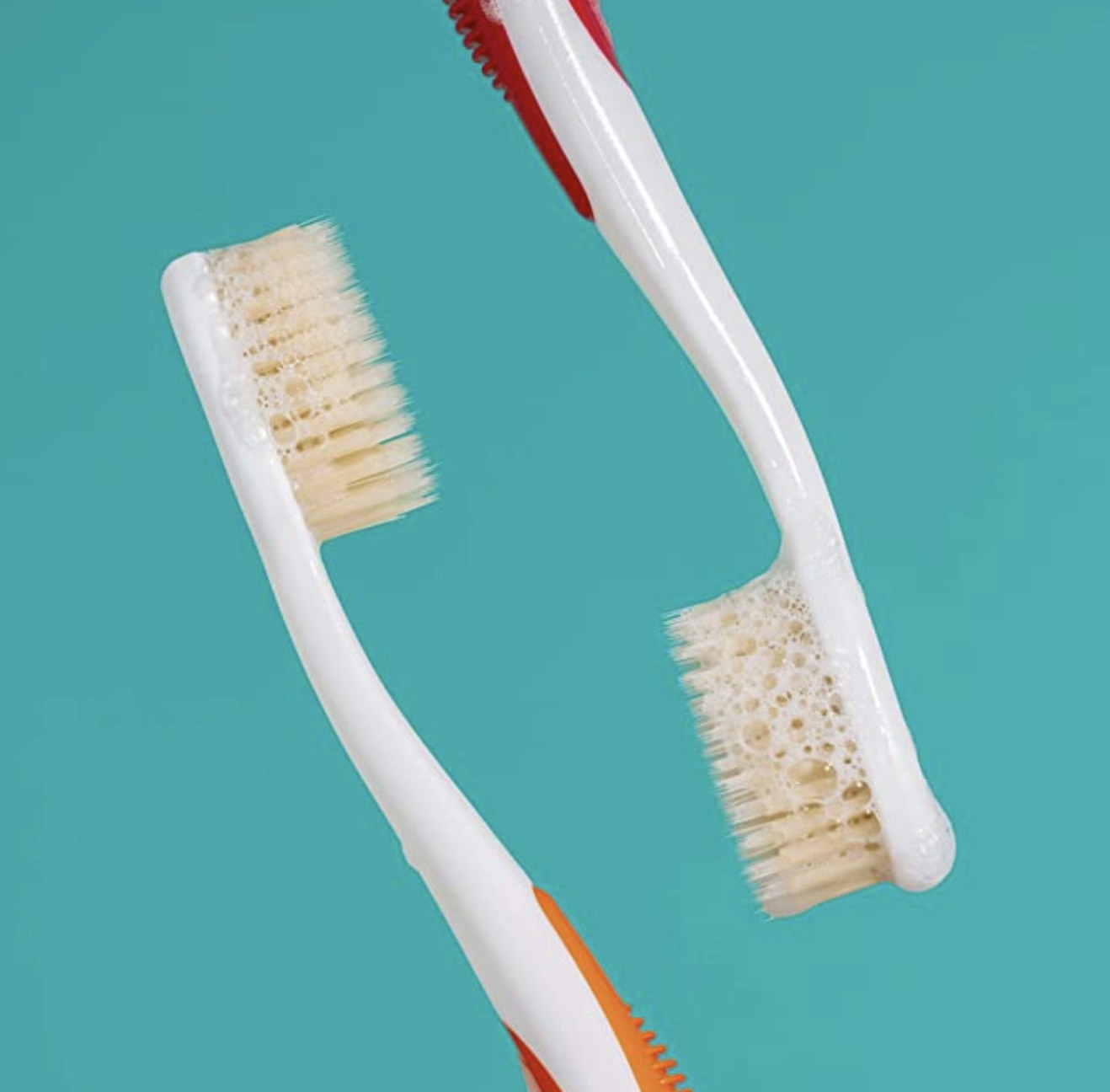 Two toothbrushes with suds on them