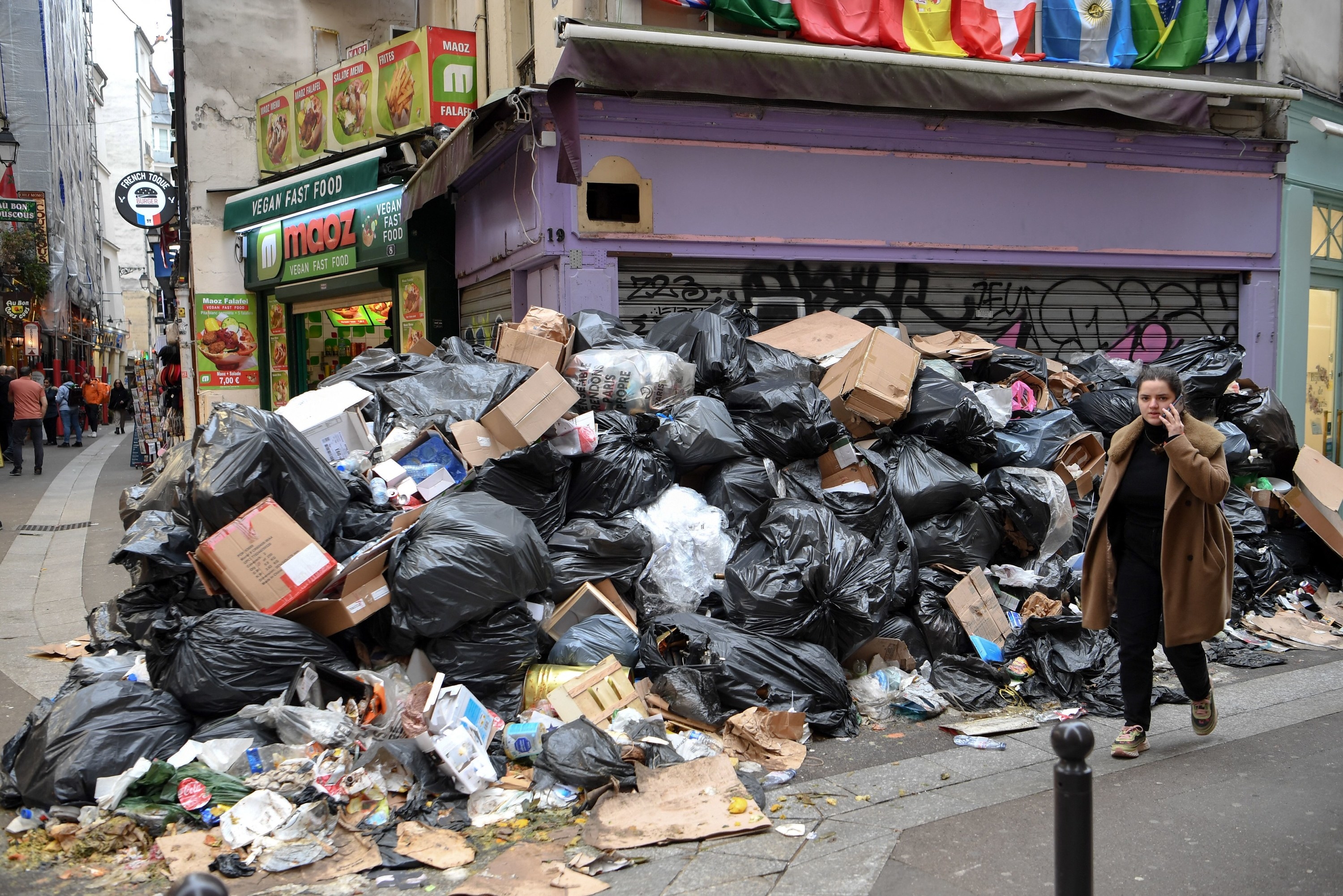 A pedestrian speaks on the phone as she walks by a pile of trash that reaches her height