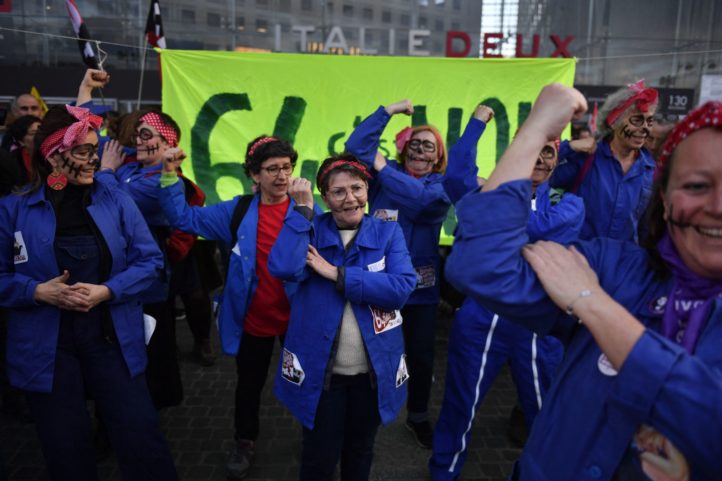 Feminist collective members wear jackets with patches and bandanas tied around their heads hold their arms up in the &quot;Rosie the Riveter&quot; pose with their faces painted like skeletons