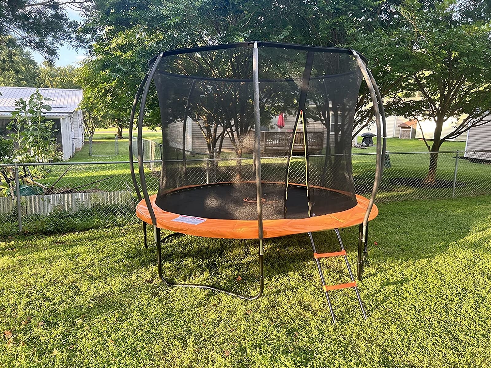 Reviewer&#x27;s photo of black trampoline with orange trim and steps in backyard setting