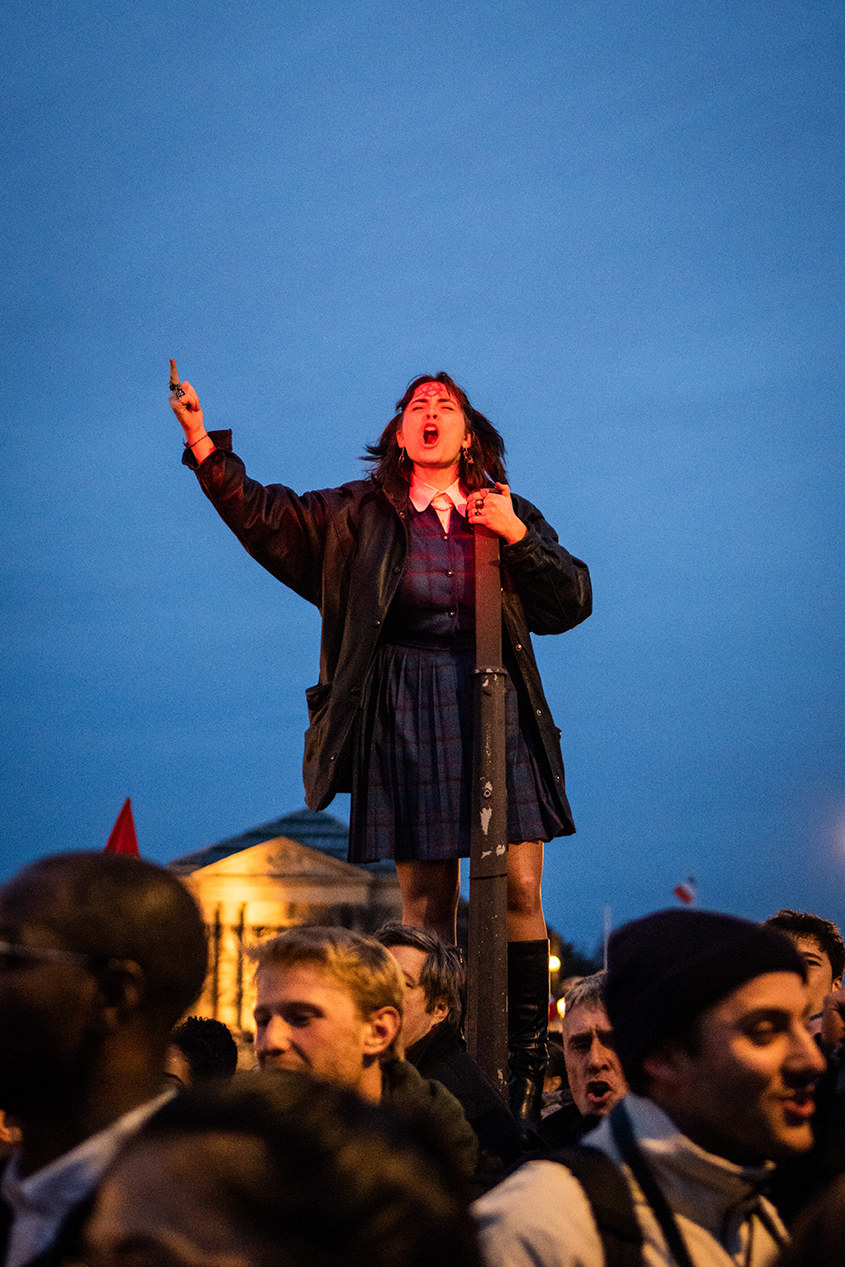 a protester climbs a pole and yells above the protesting crowd