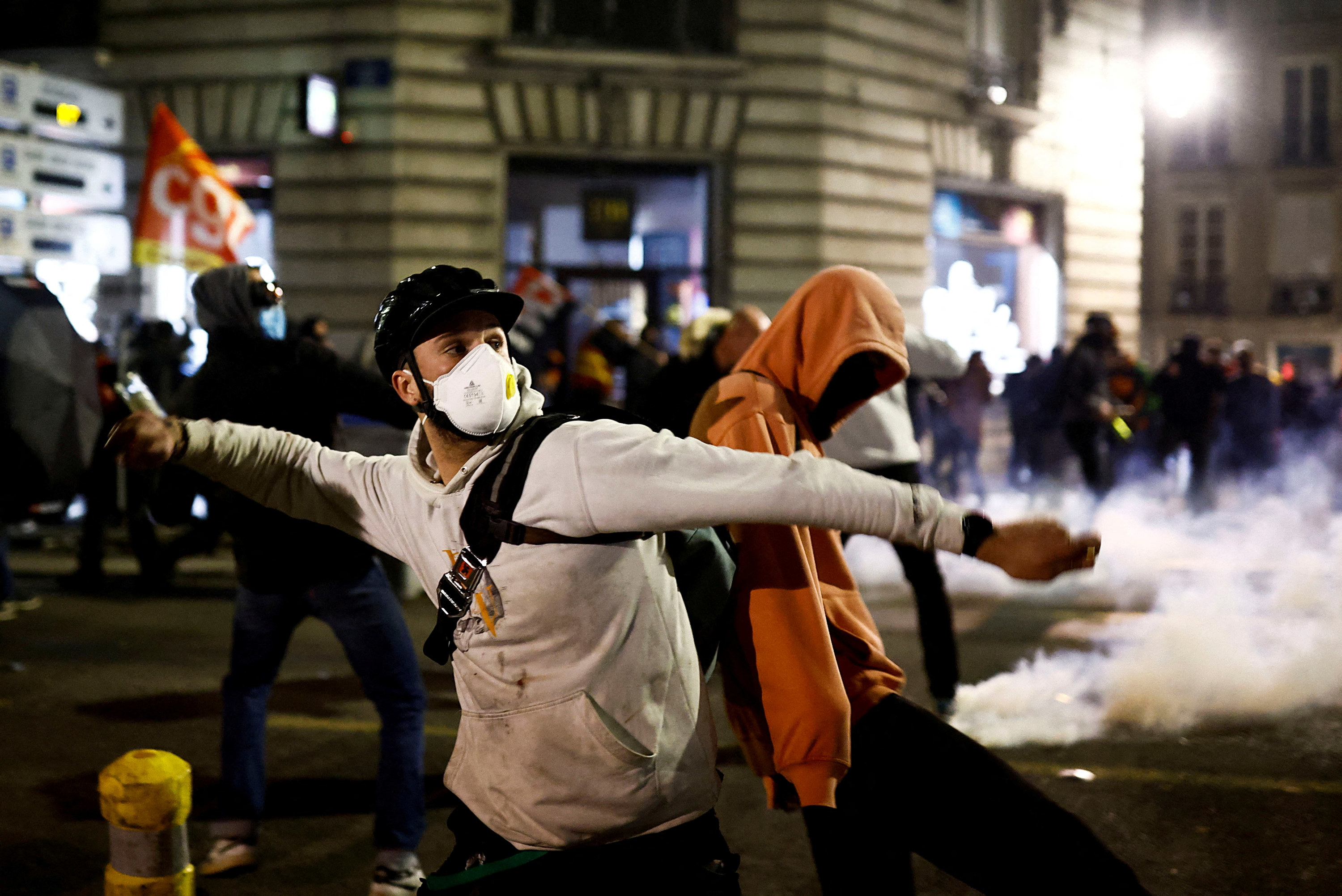 a protester wearing a bike helment and a mask throws projectiles at the police