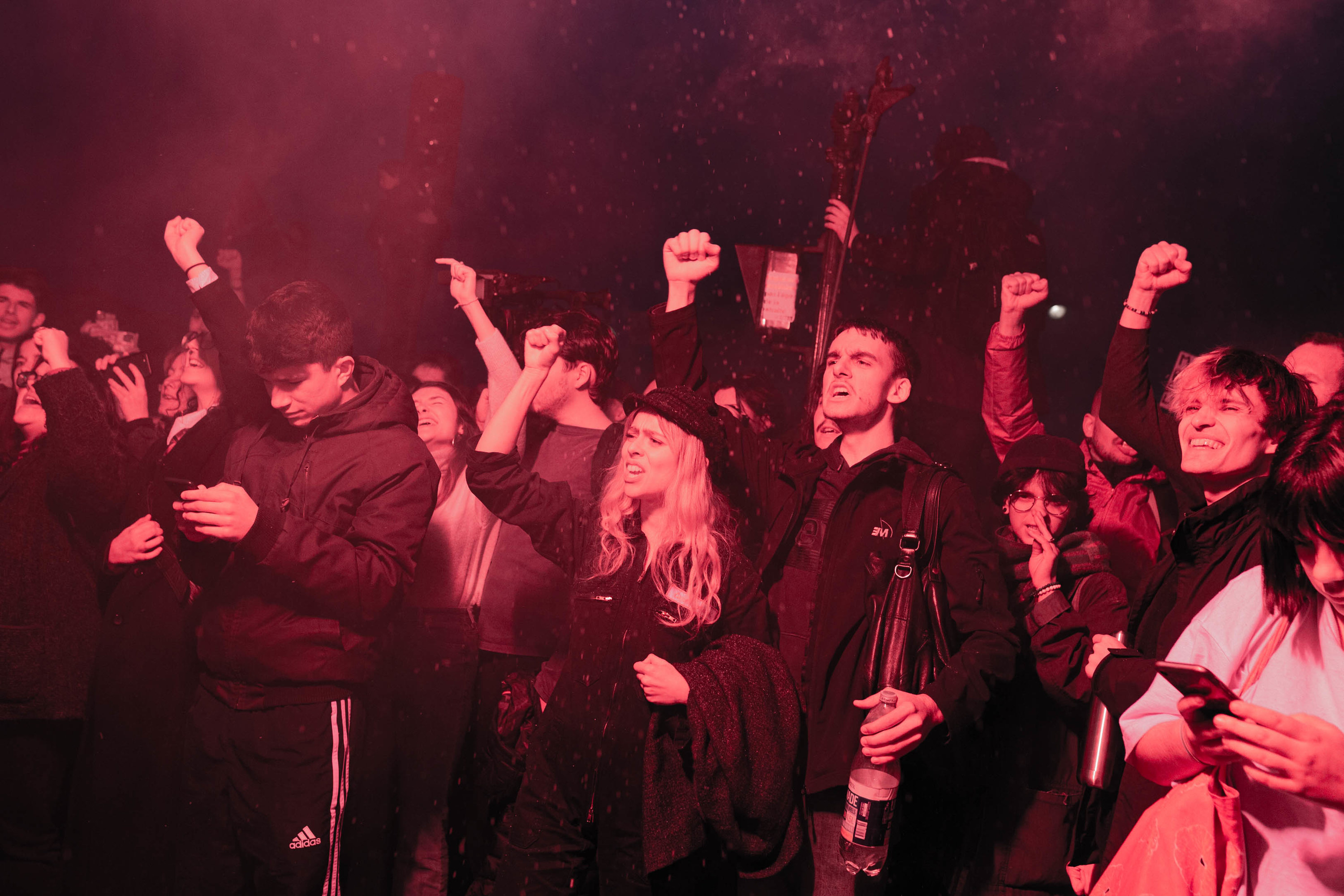 a group at night raises their arms and chants are illuminated by a flare