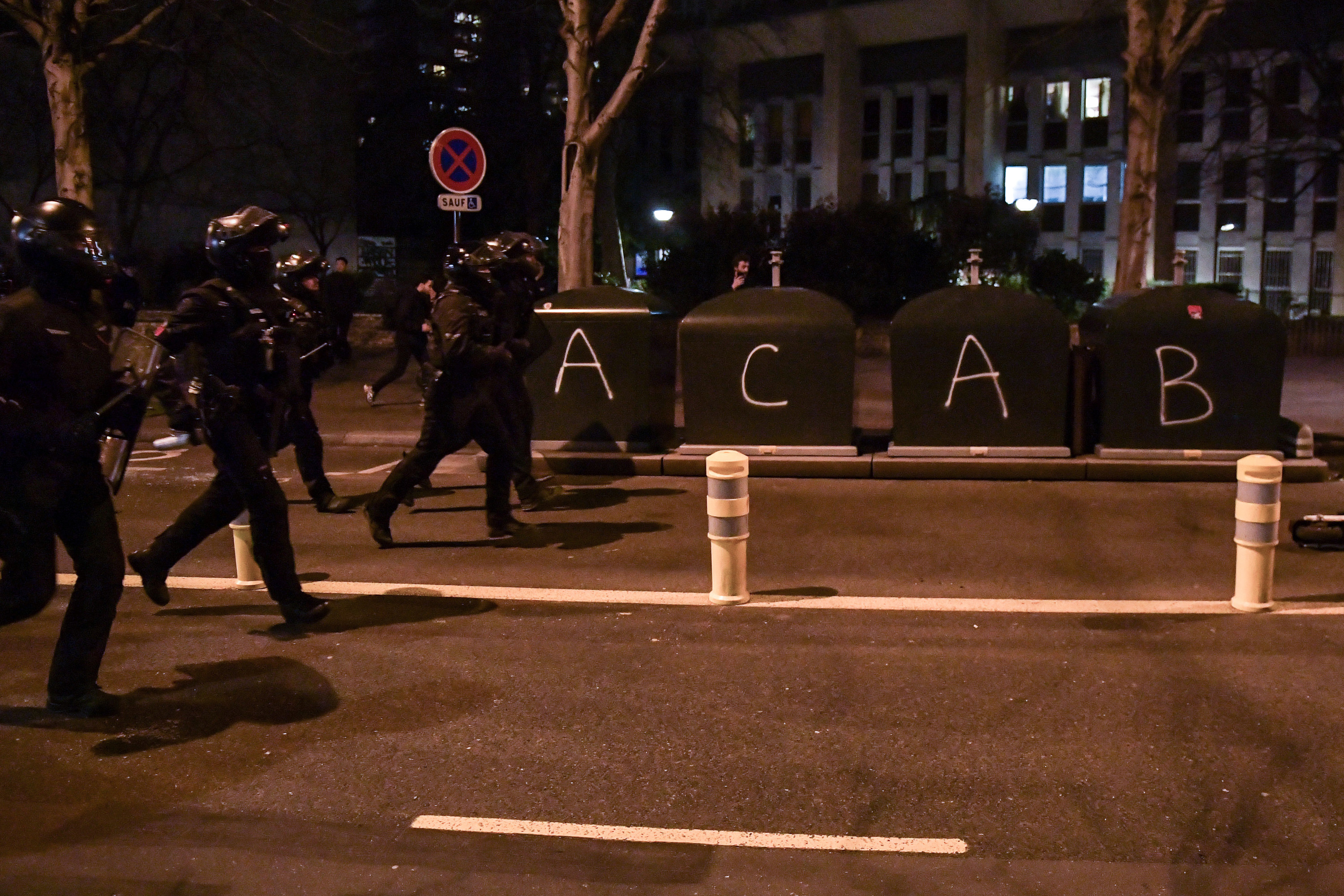 Riot police run down the street that has been vandalized with the tag &quot;ACAB&quot;