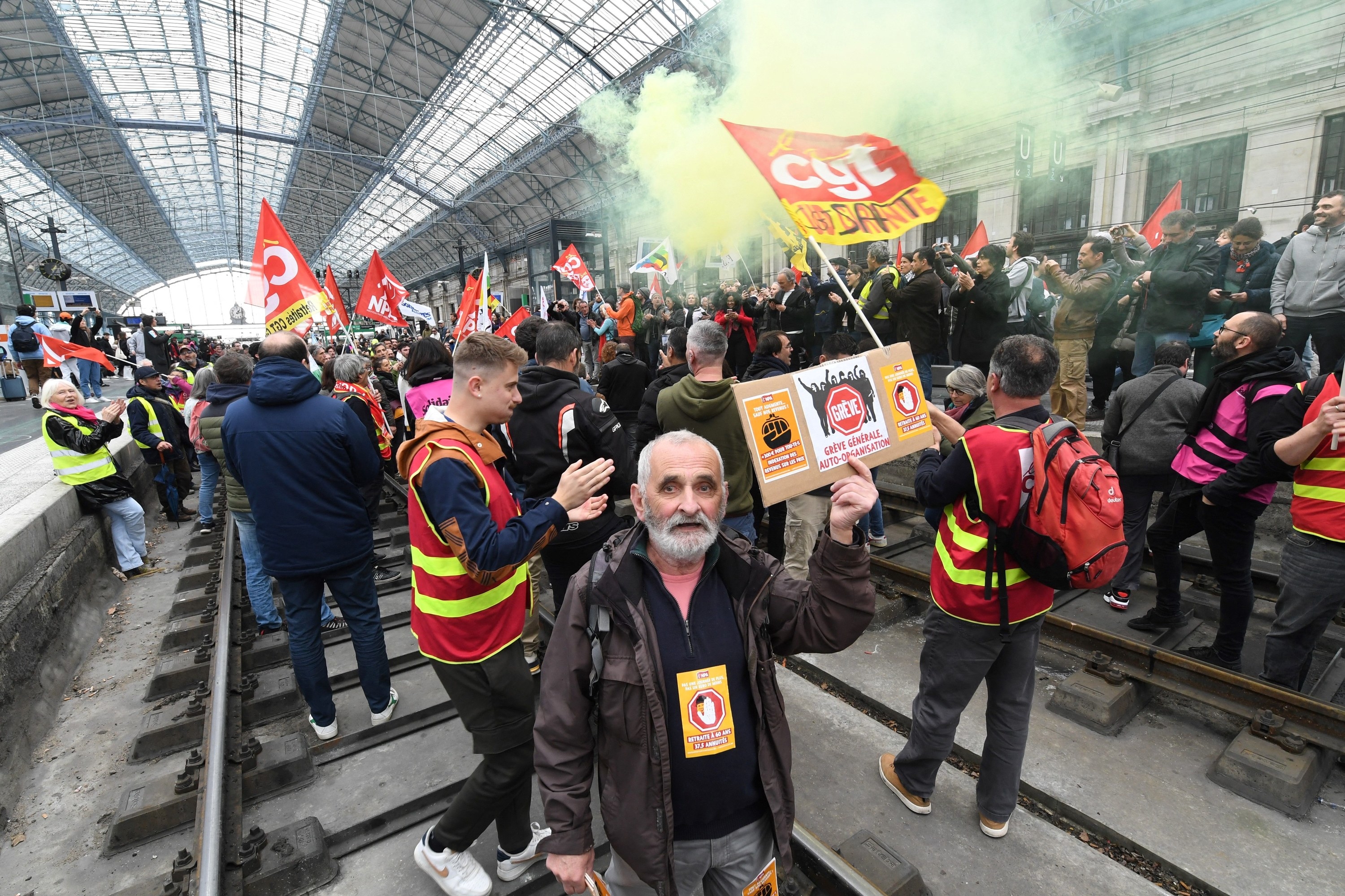 Hundreds of railway union members and supporters holding flags and wearing high-visibility vests fill a train station