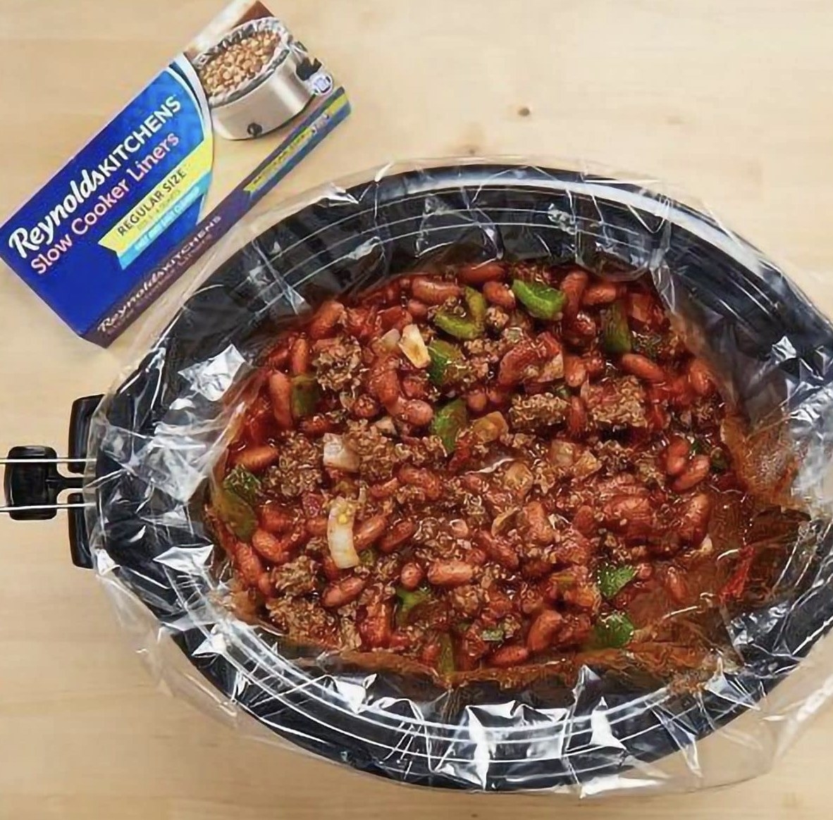 A slow cooker with liner and chili in it