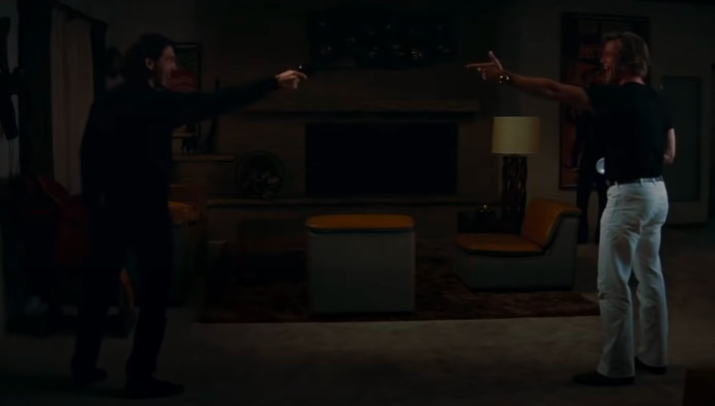A man aims a gun at another man, who holds up his hand in a finger gun