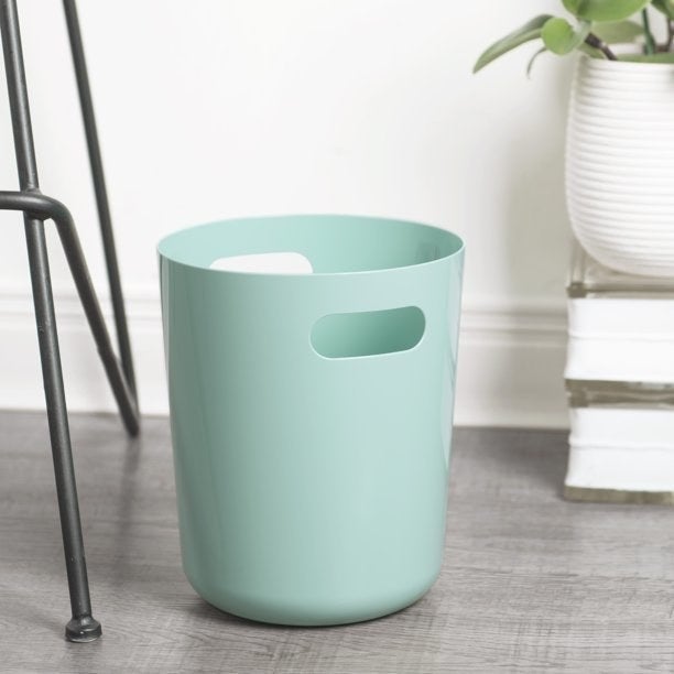 a blue wastebasket on a wood floor next to a chair or desk
