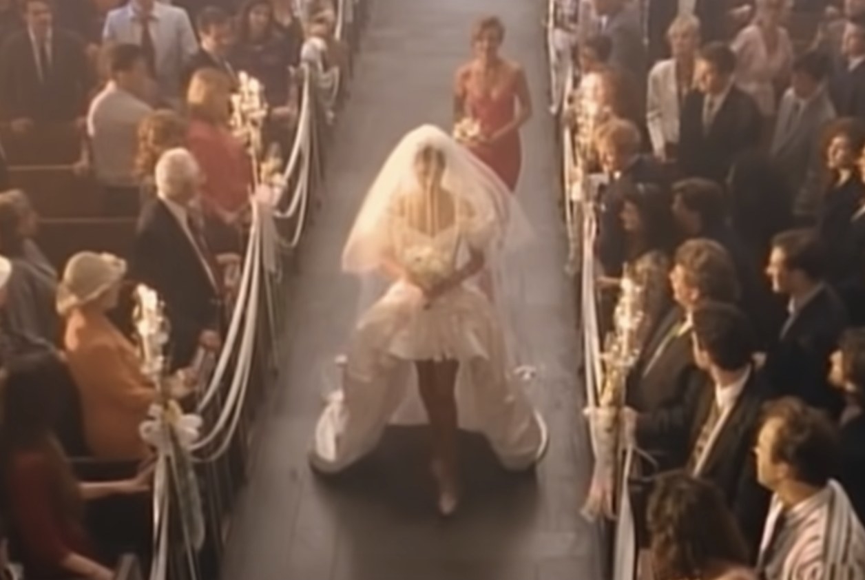 A woman walks down the aisle in a short dress and veil