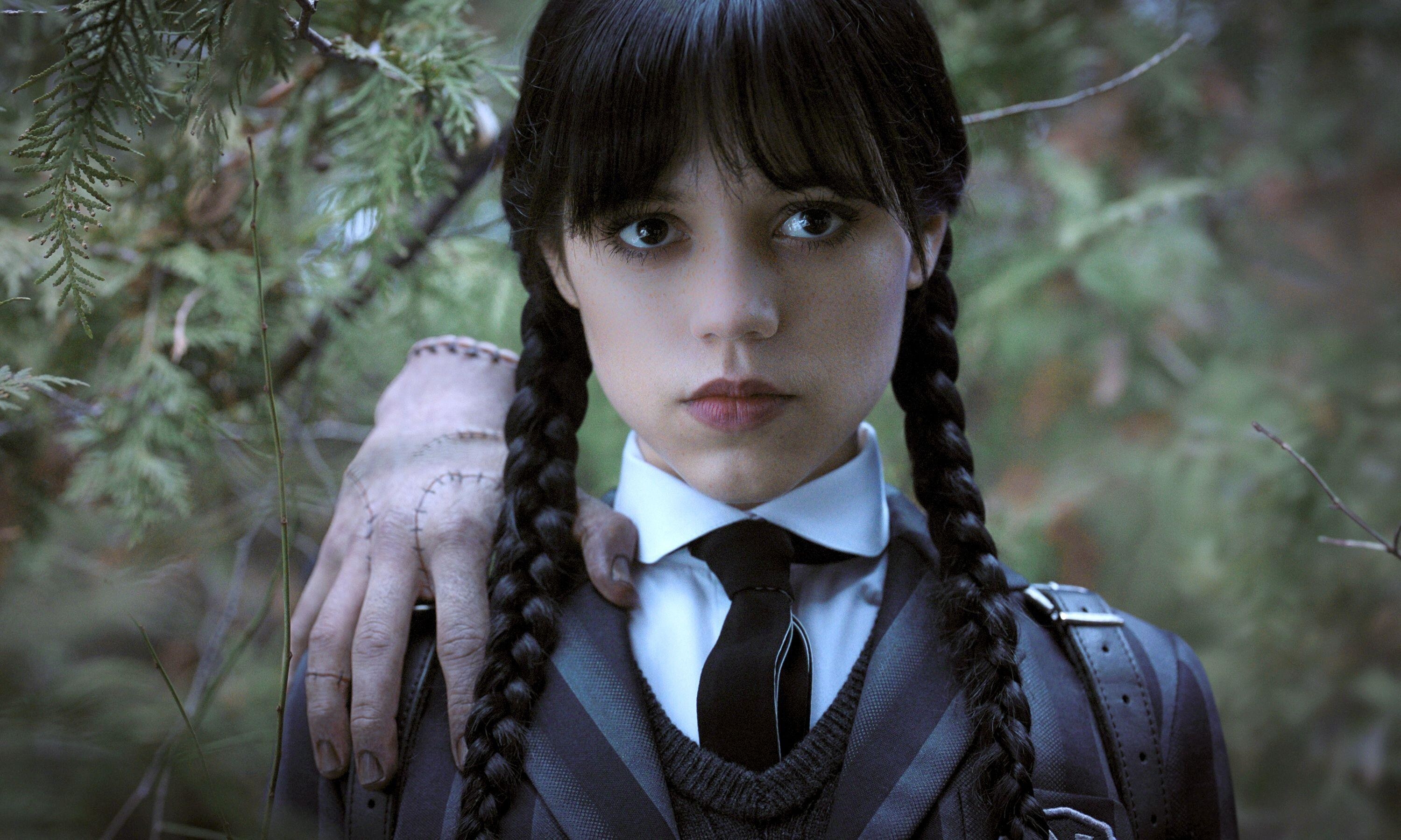 A severed hand rests on the shoulders of Jenna Ortega as Wednesday Addams