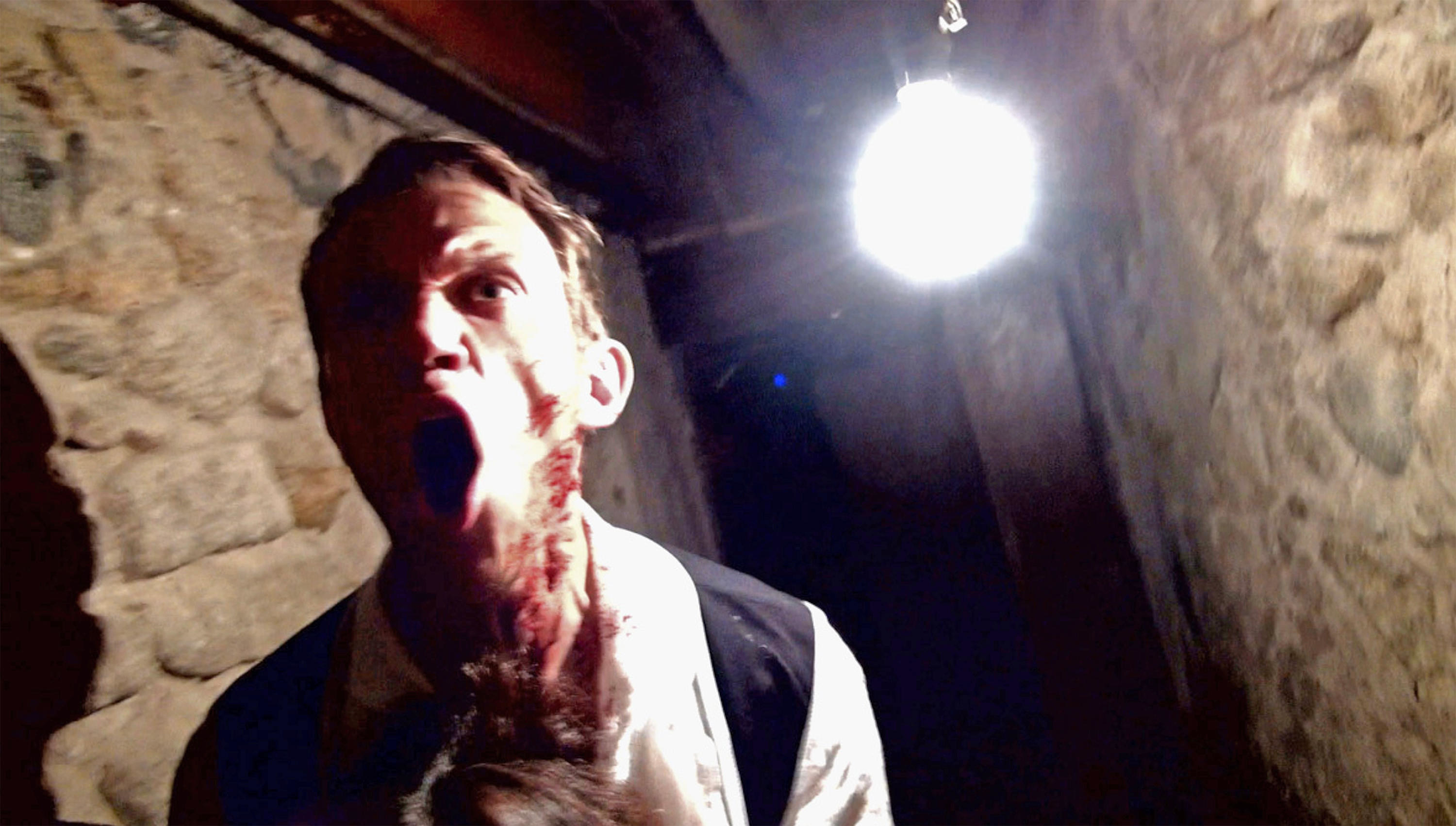 A bloodied man screams in a tight stone hallway