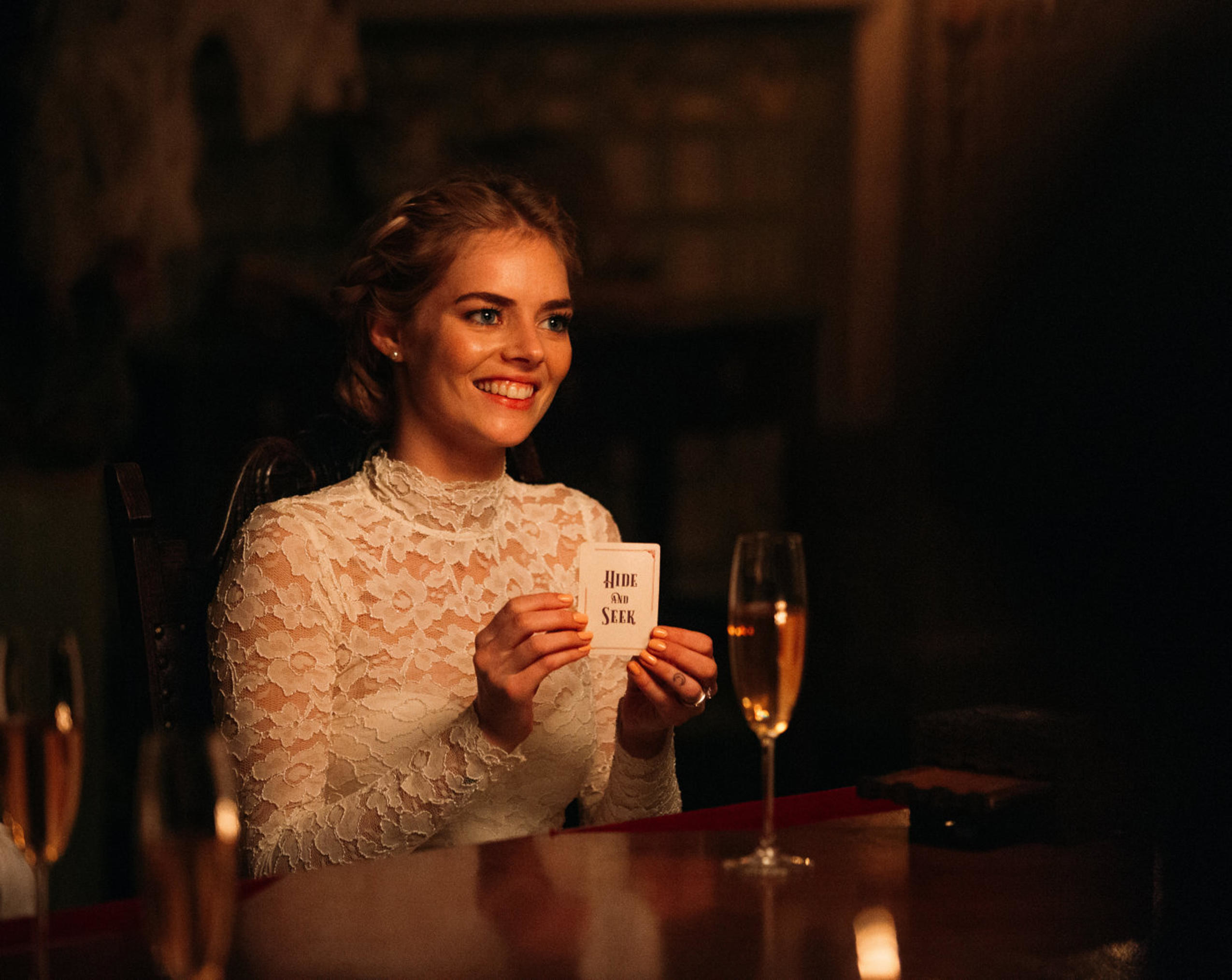 Samara Weaving in a wedding dress smiles and holds up a novelty card
