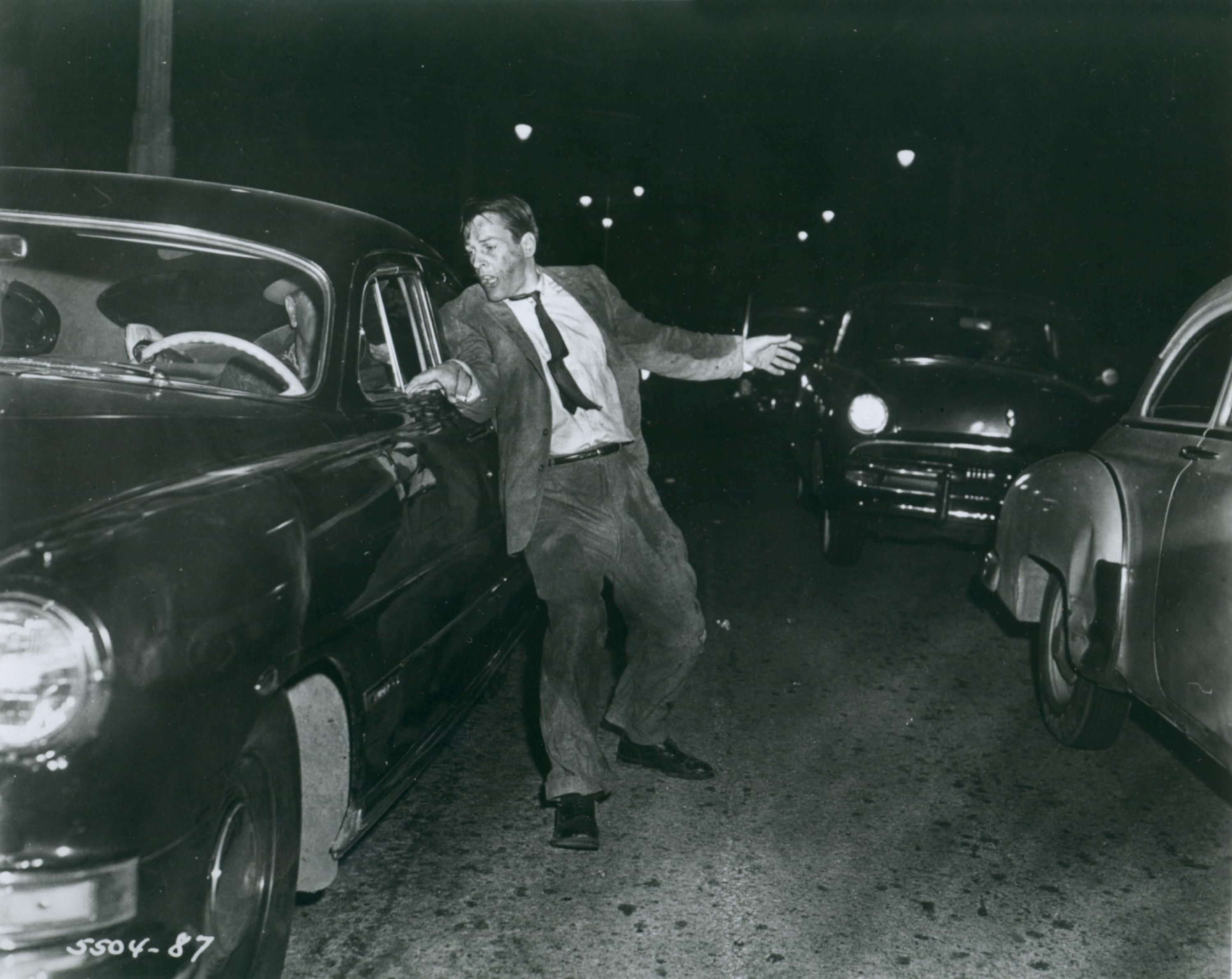 A haggard man in a suit bounces between cars in traffic