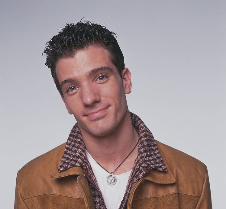 A closeup of a younger JC wearing a plain t-shirt, zip-up, and leather jacket