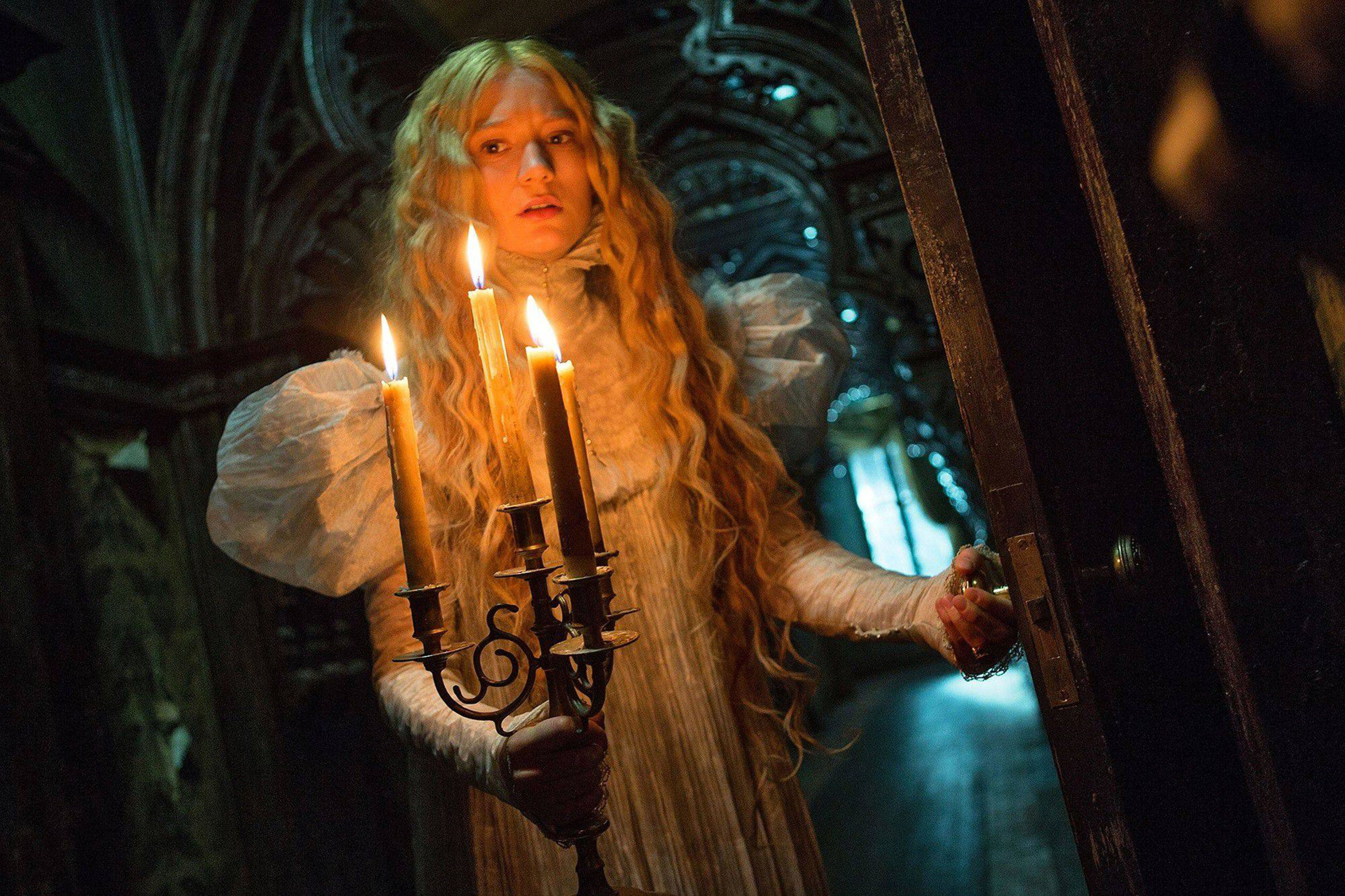 Mia Wasikowska walks down a dark mansion hallway with a candelabra