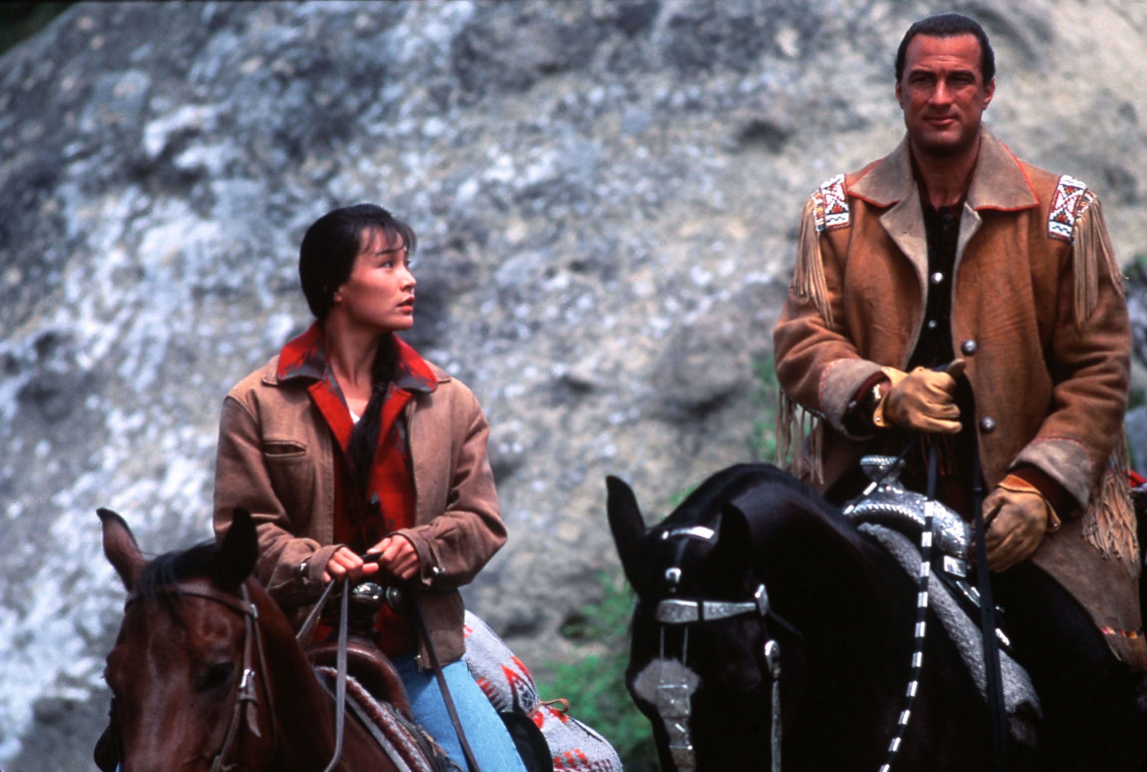 Joan Chen and Steven Seagal ride horses in a mountain range