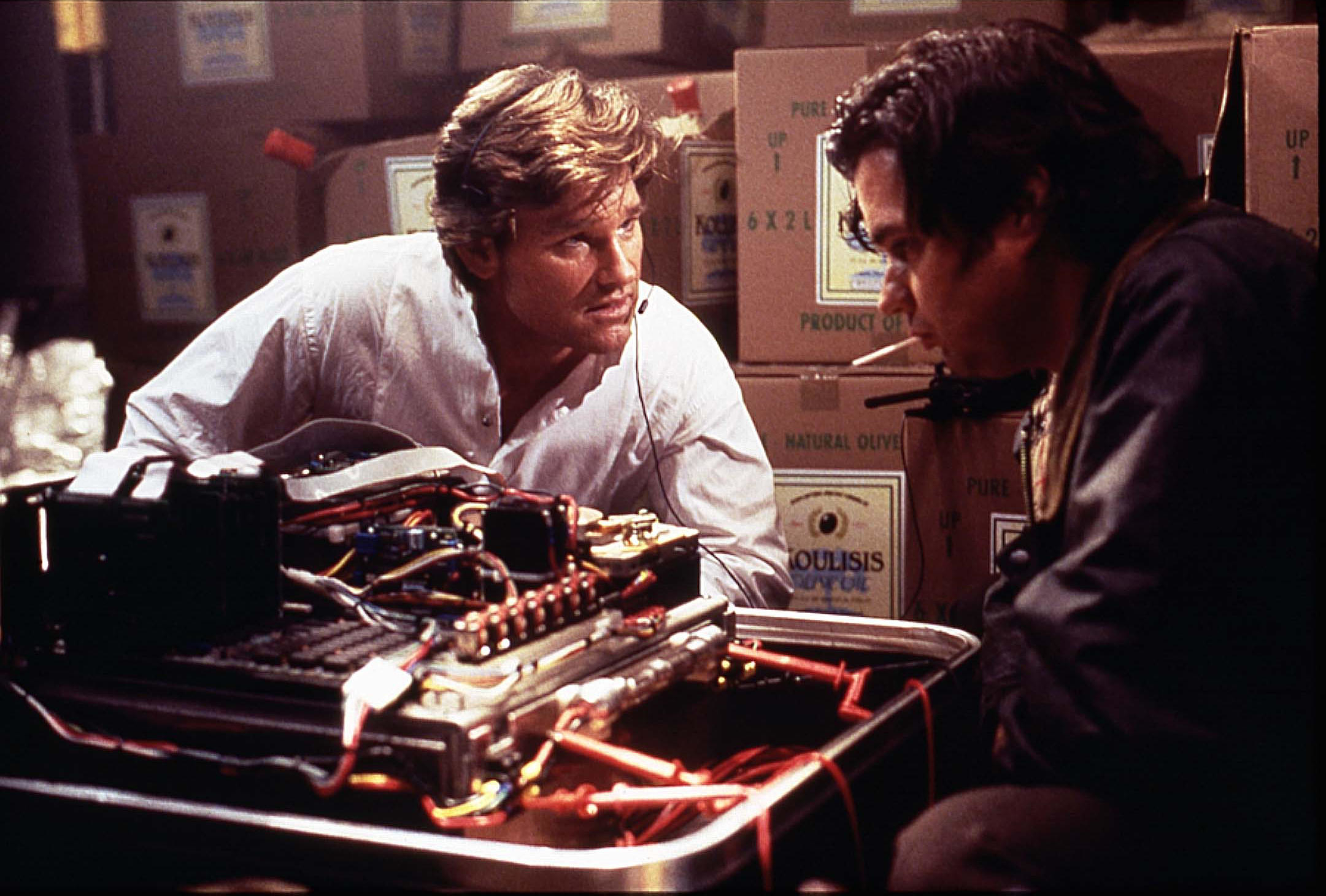 Kurt Russell talks with Oliver Platt near a mechanical device