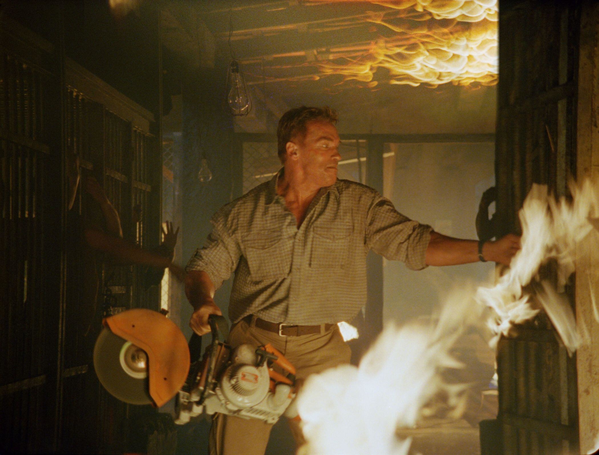 Arnold Schwarzenegger handles a powersaw in a fire