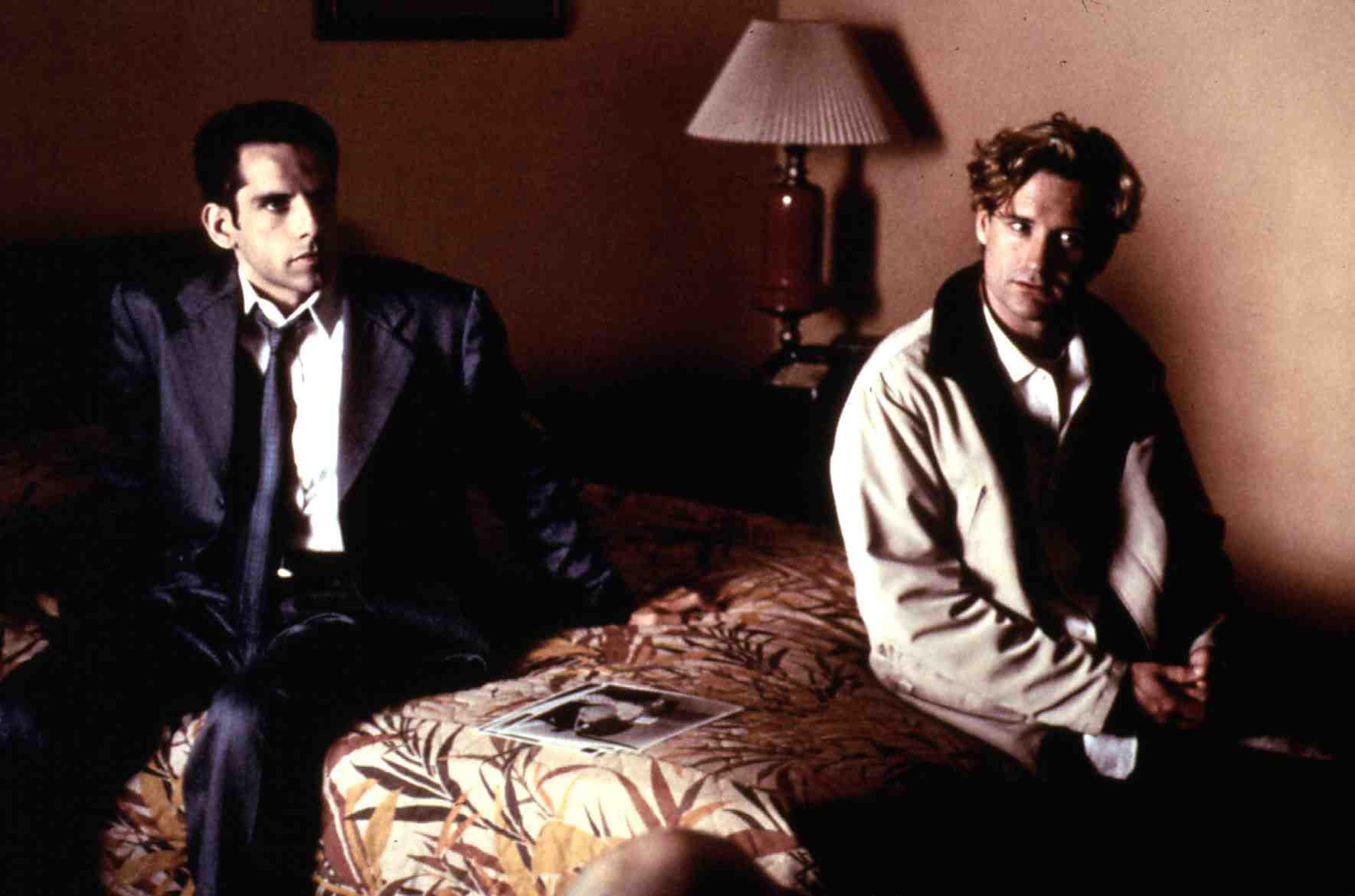 Ben Stiller and Bill Pullman sit on a bed near some photographs