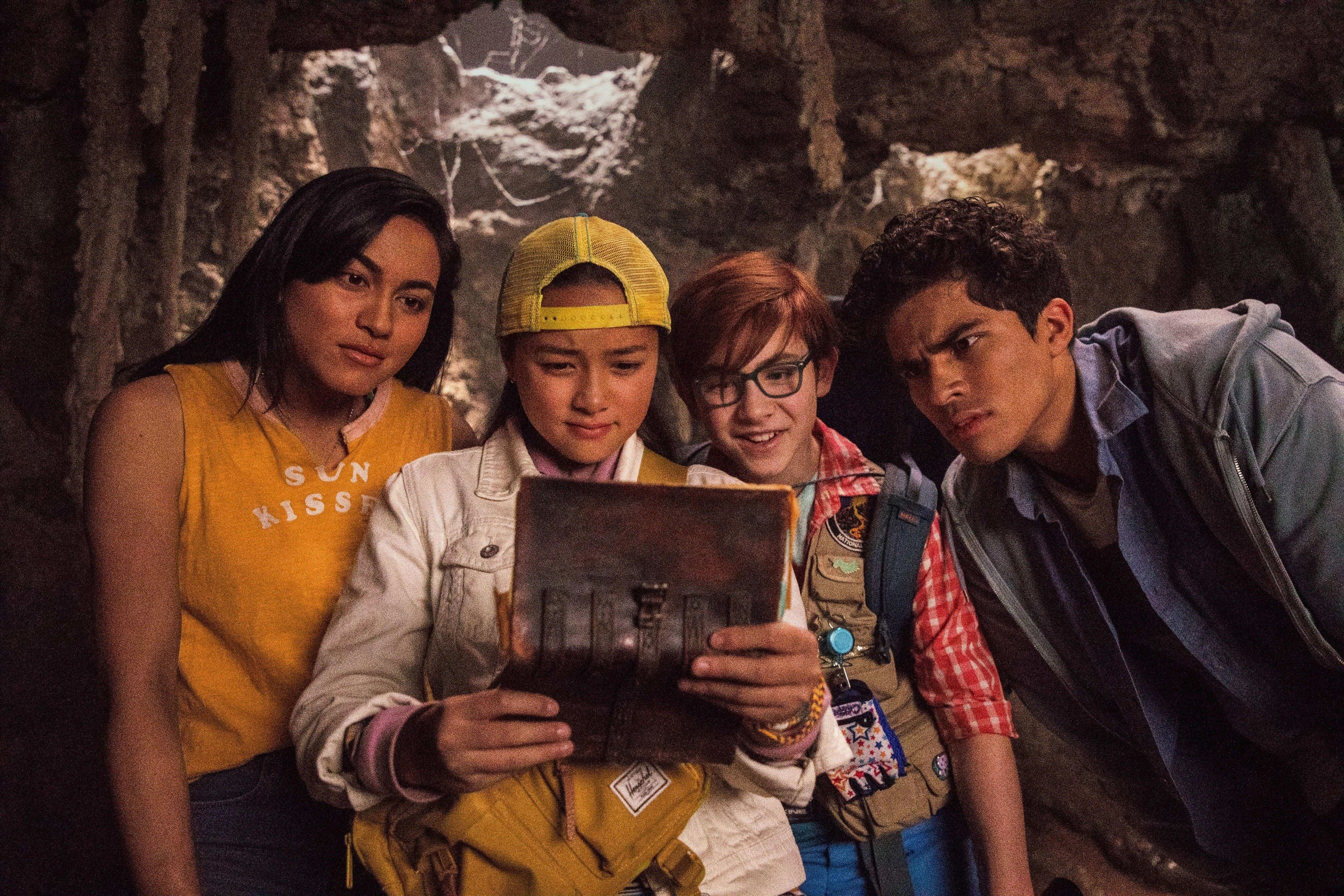 Four young people stare at an old book in a cave