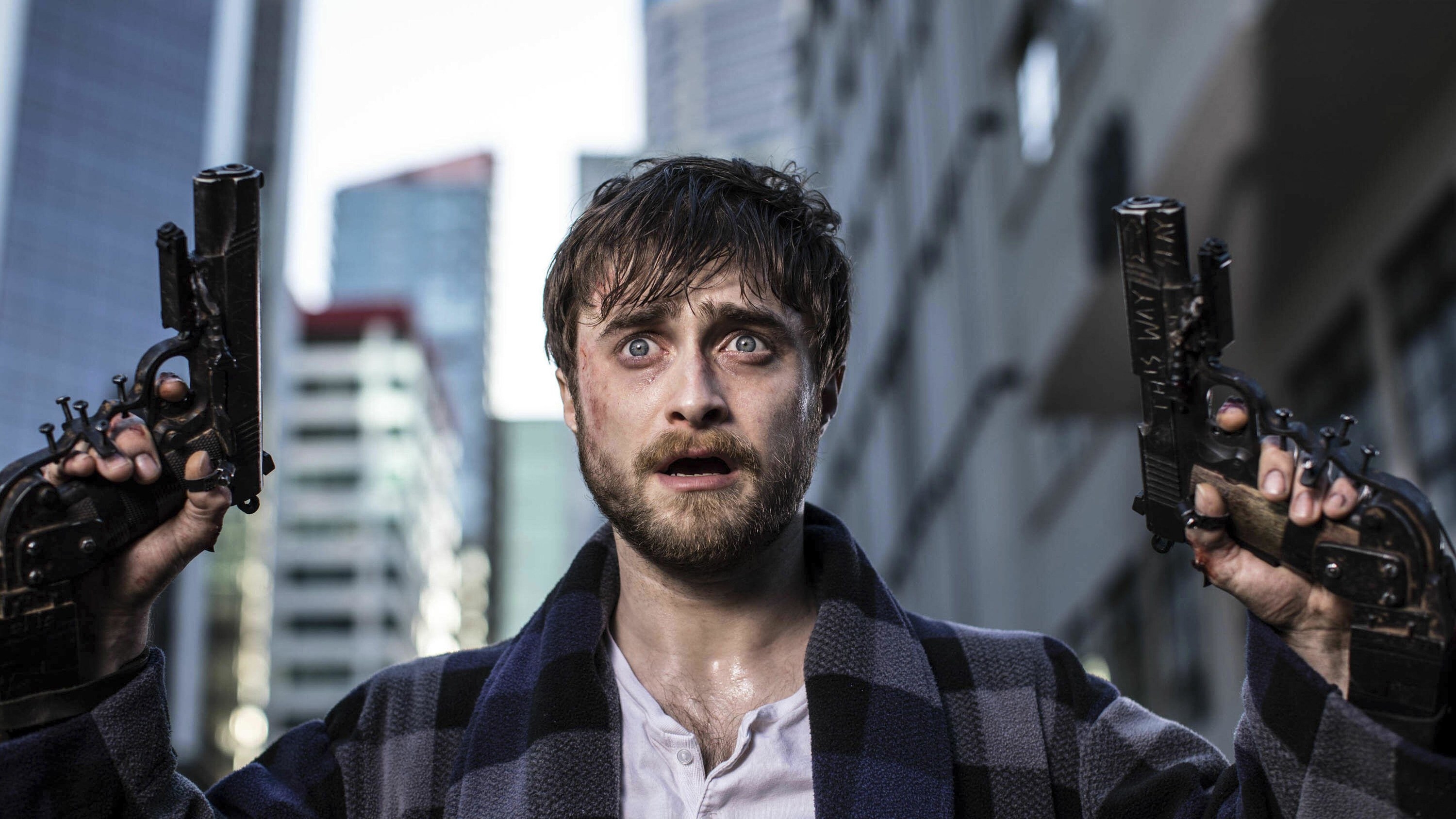 Daniel Radcliffe holds up two guns nailed into his fingers on the city streets