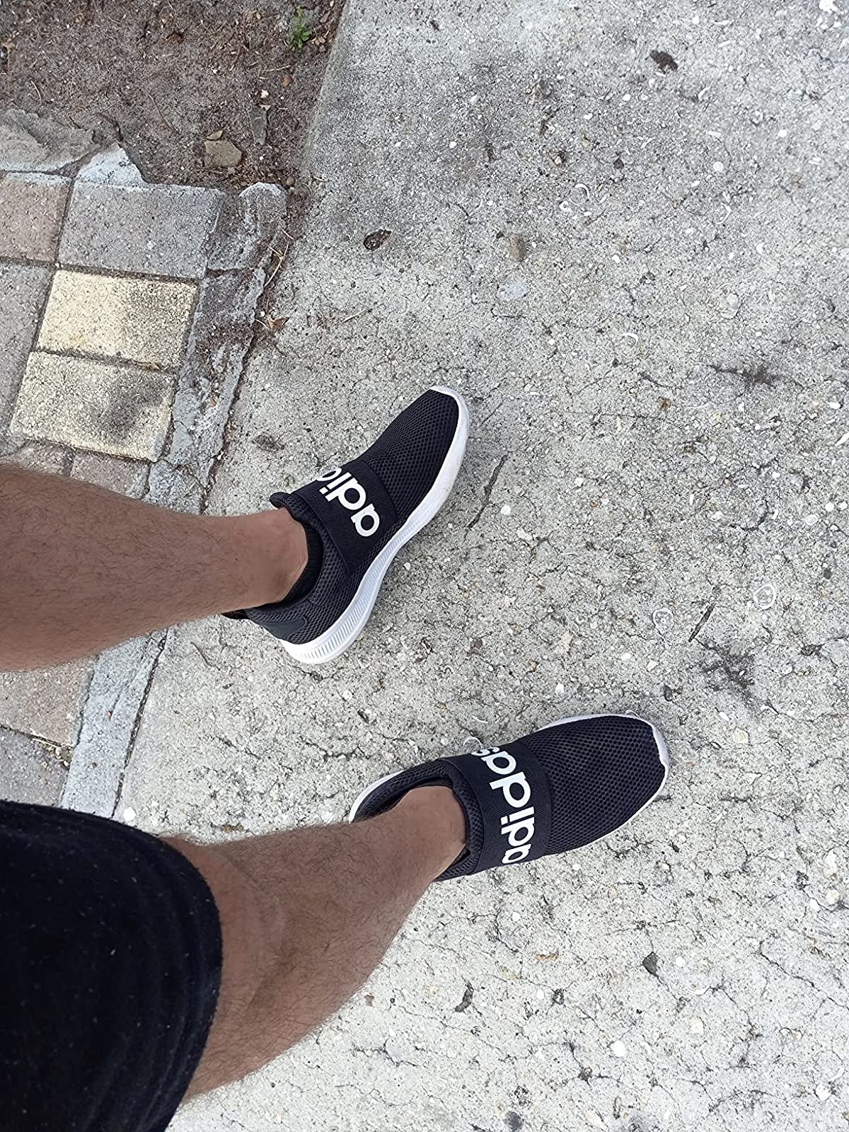Reviewer wearing black slip on shoe with white adidas logo across front strap