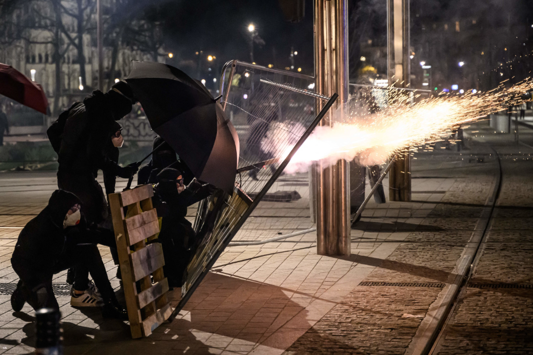 protesters fire something with a shower of sparks and shield themselves from police using wooden boards and umbrellas