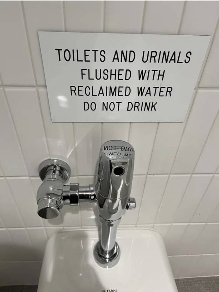 sign above a toilet that says &quot;toilets and urinals flushed with reclaimed water. do not drink.&quot;