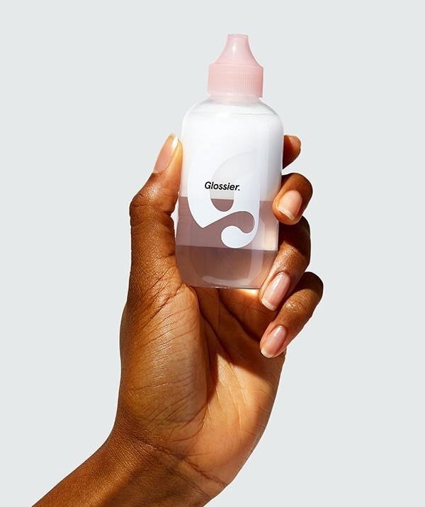 someone holding up a bottle of the glossier oil cleanser