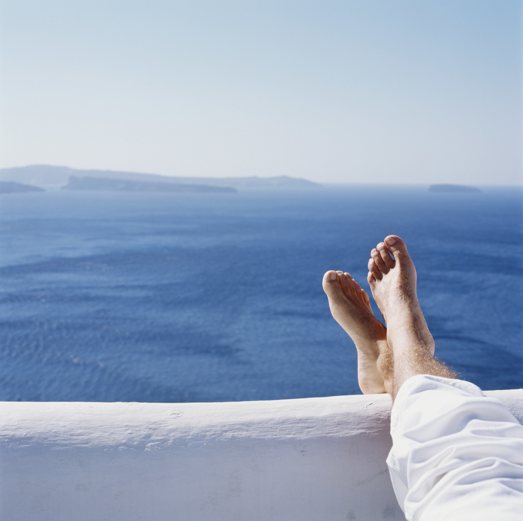 Man resting legs on wall overlooking ocean