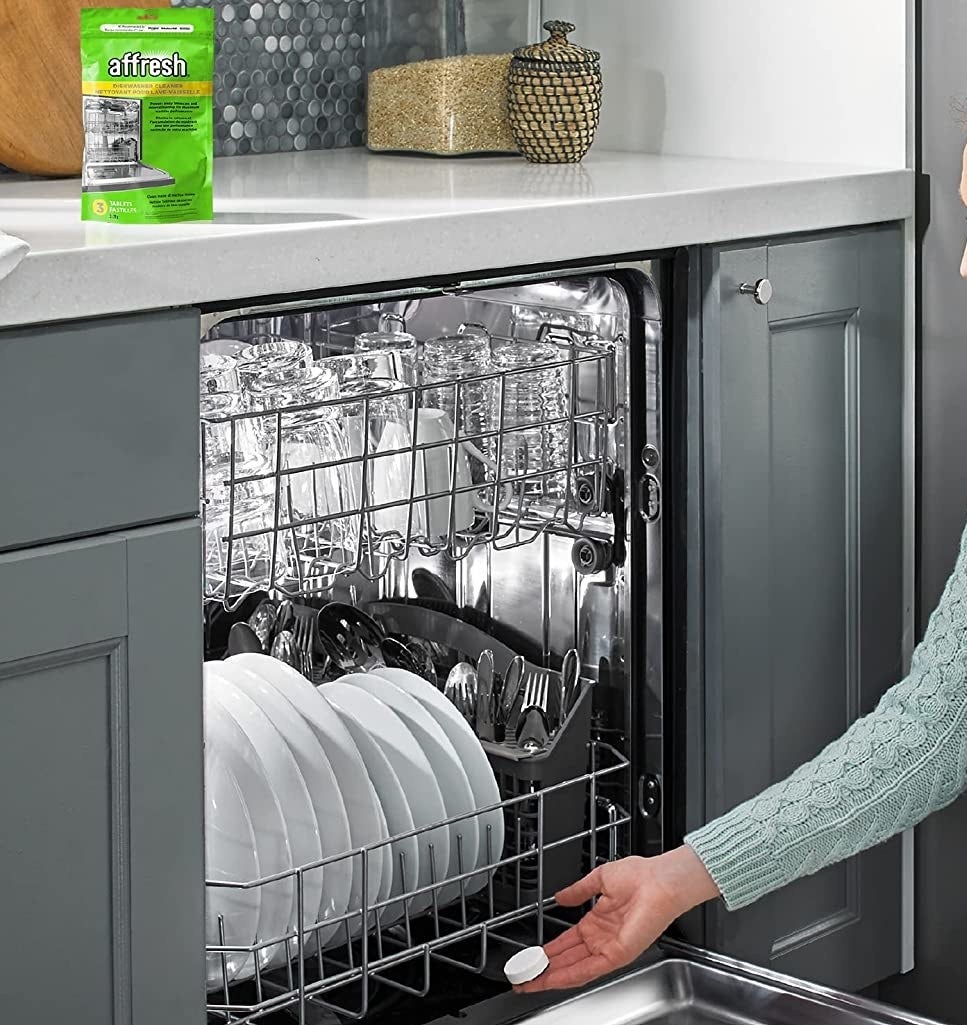 a person putting a dishwasher cleaner tablet into a dishwasher