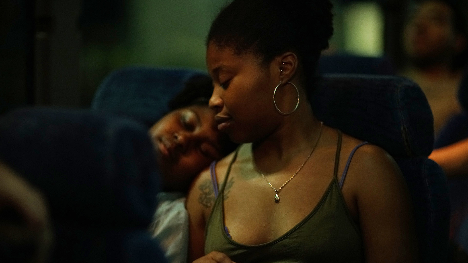 dominique fishback sitting in a seat on the bus as she looks down at her sibling who fell asleep on her shoulder