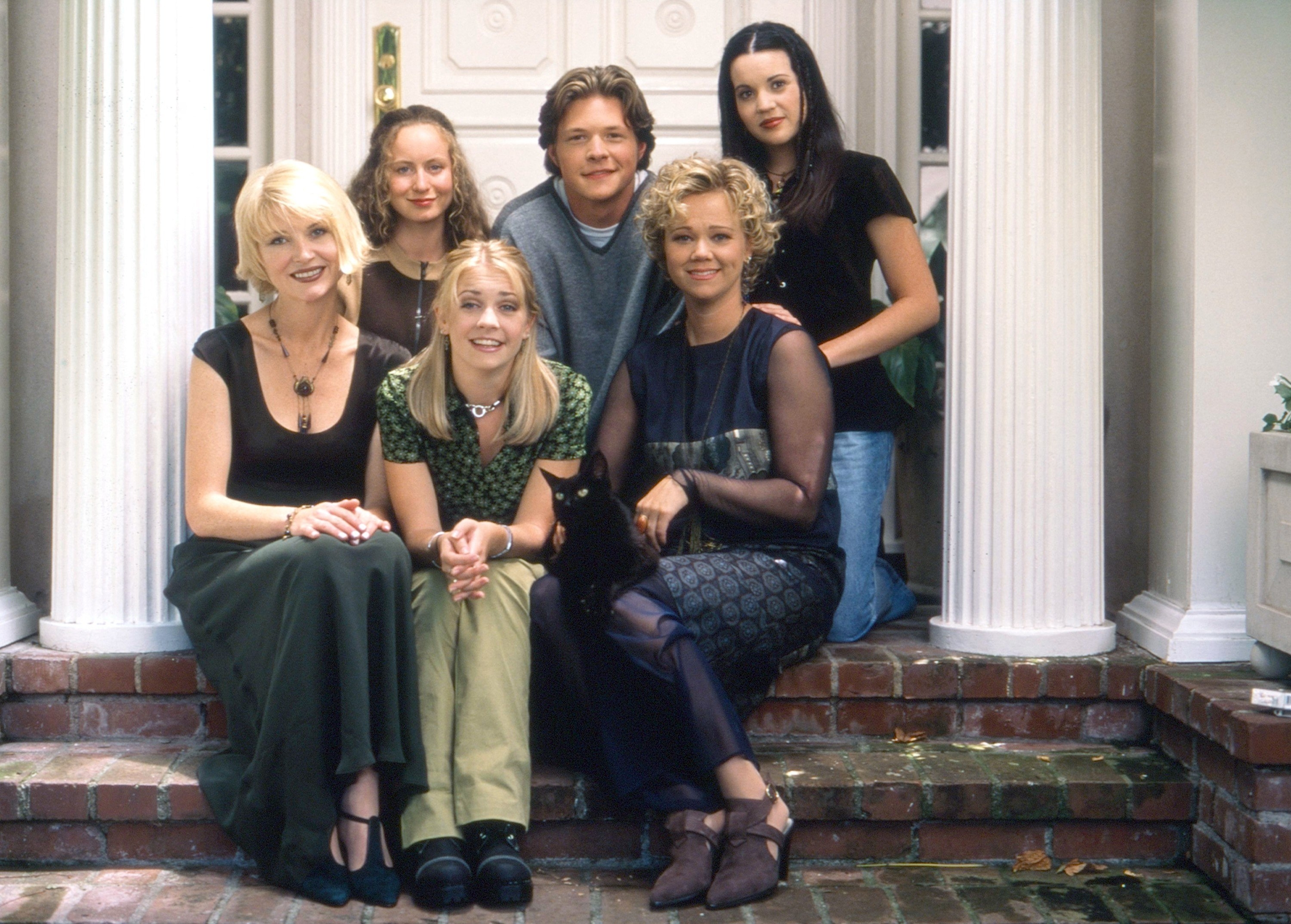 A throwback photo of the cast sitting on the steps of a home