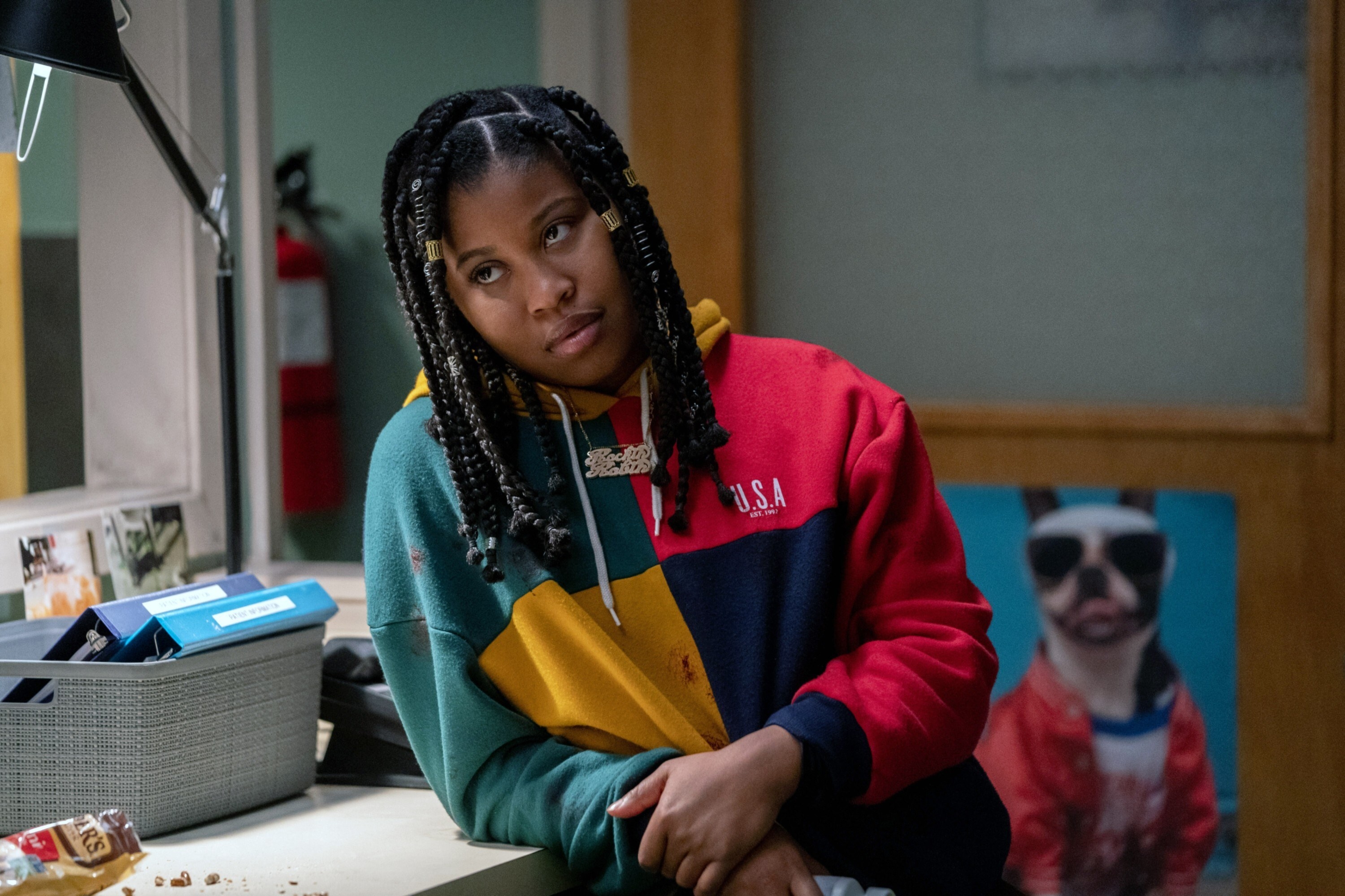 dominique fishback wearing a color-block sweatshirt and box braids as she leans on a counter in a classroom