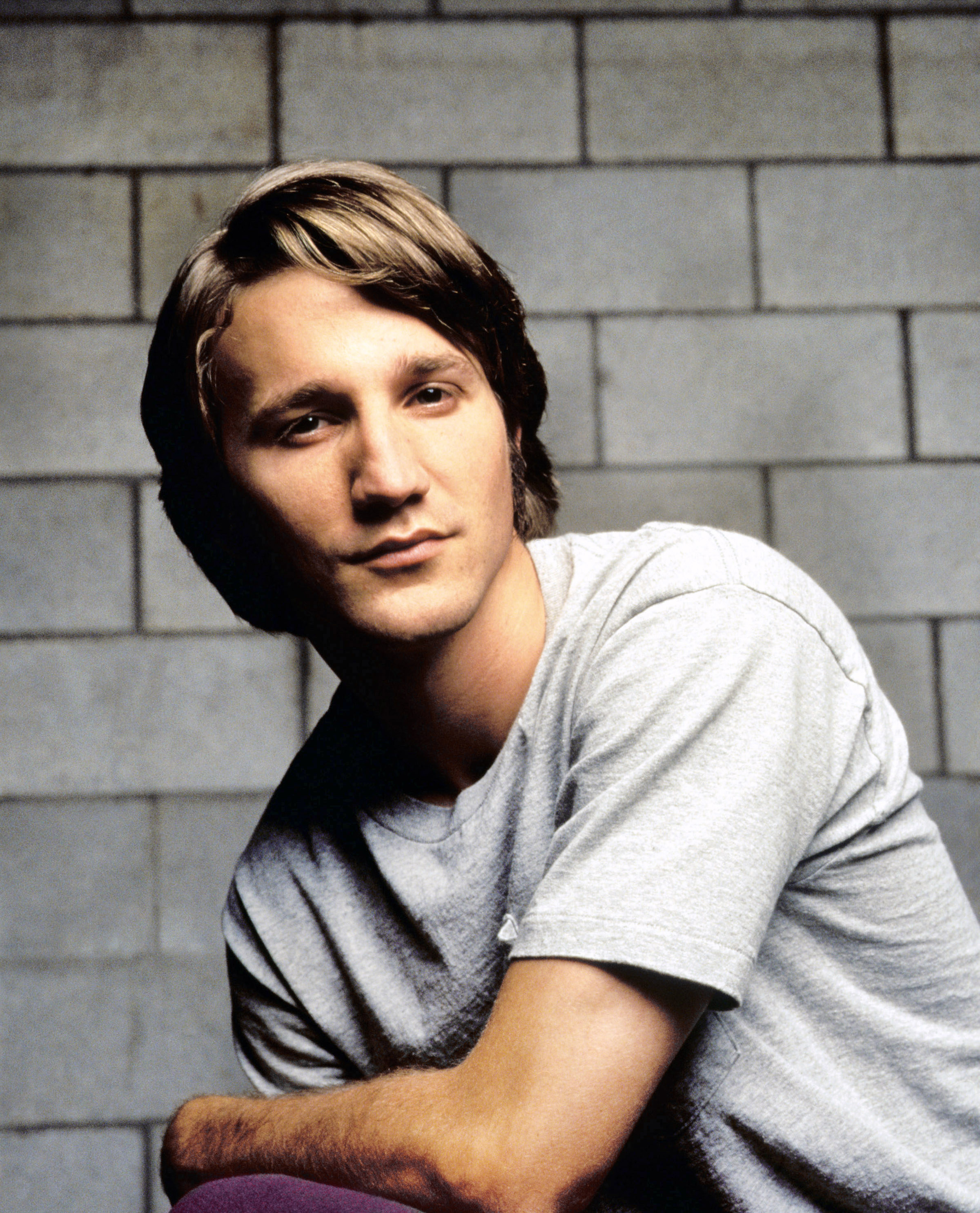 A young Breckin sitting in a chair backwards with a brick wall behind him