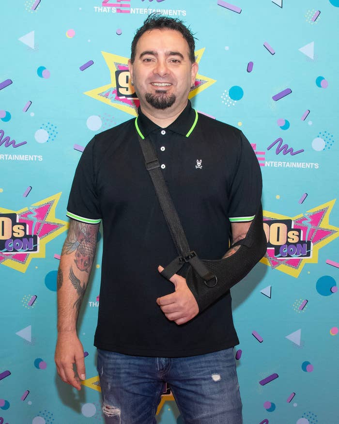 Chris Kirkpatrick smiles on the red carpet of 90s Con. His left arm is in a slin