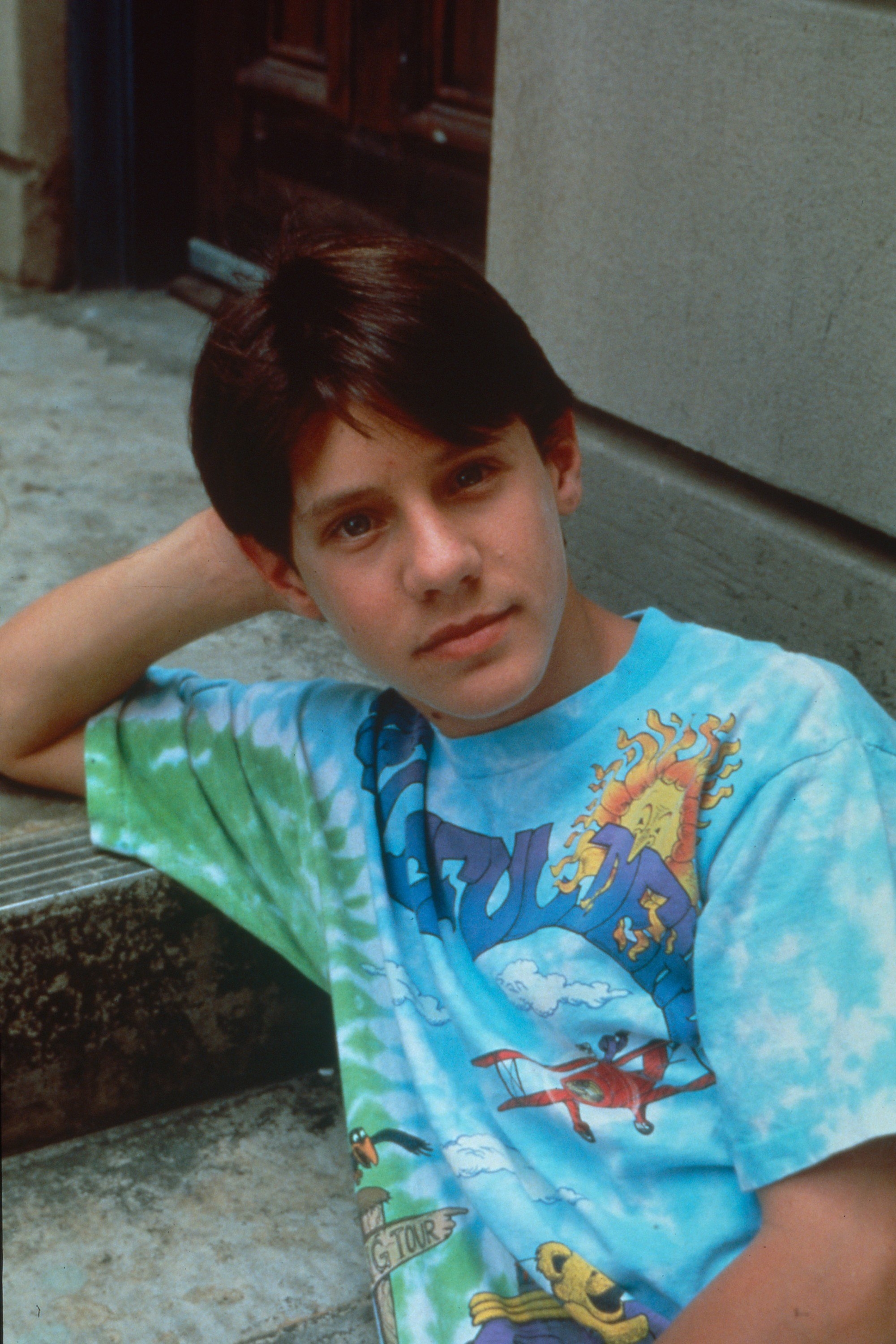 A young Omri is sitting on a set of steps outside