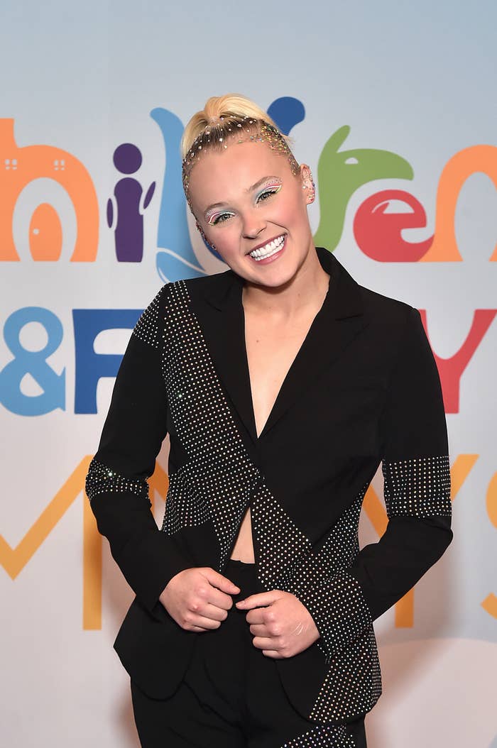 JoJo smiling widely at a red carpet event while rocking a bejeweled ponytail