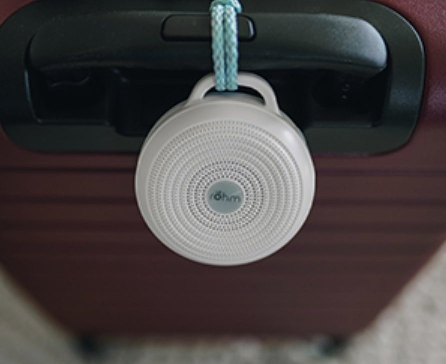 the small circular noise machine attached to the handle of a suitcase