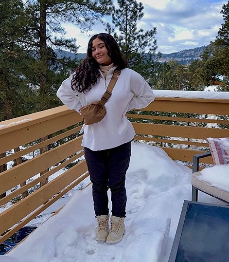reviewer posing in snow wearing the belt bag in caramel